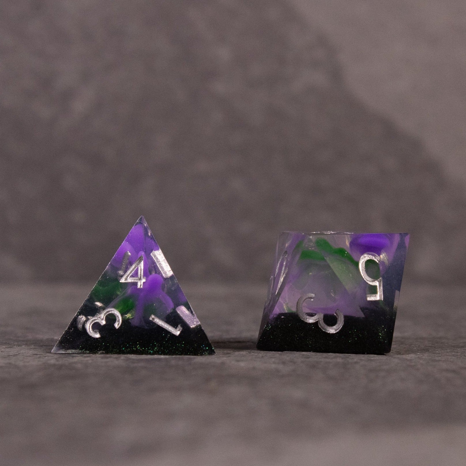 Witch's Brew Dice Set - Sharp-edged purple and green tetrahedron and cube dice with white numbering and swirling color design.