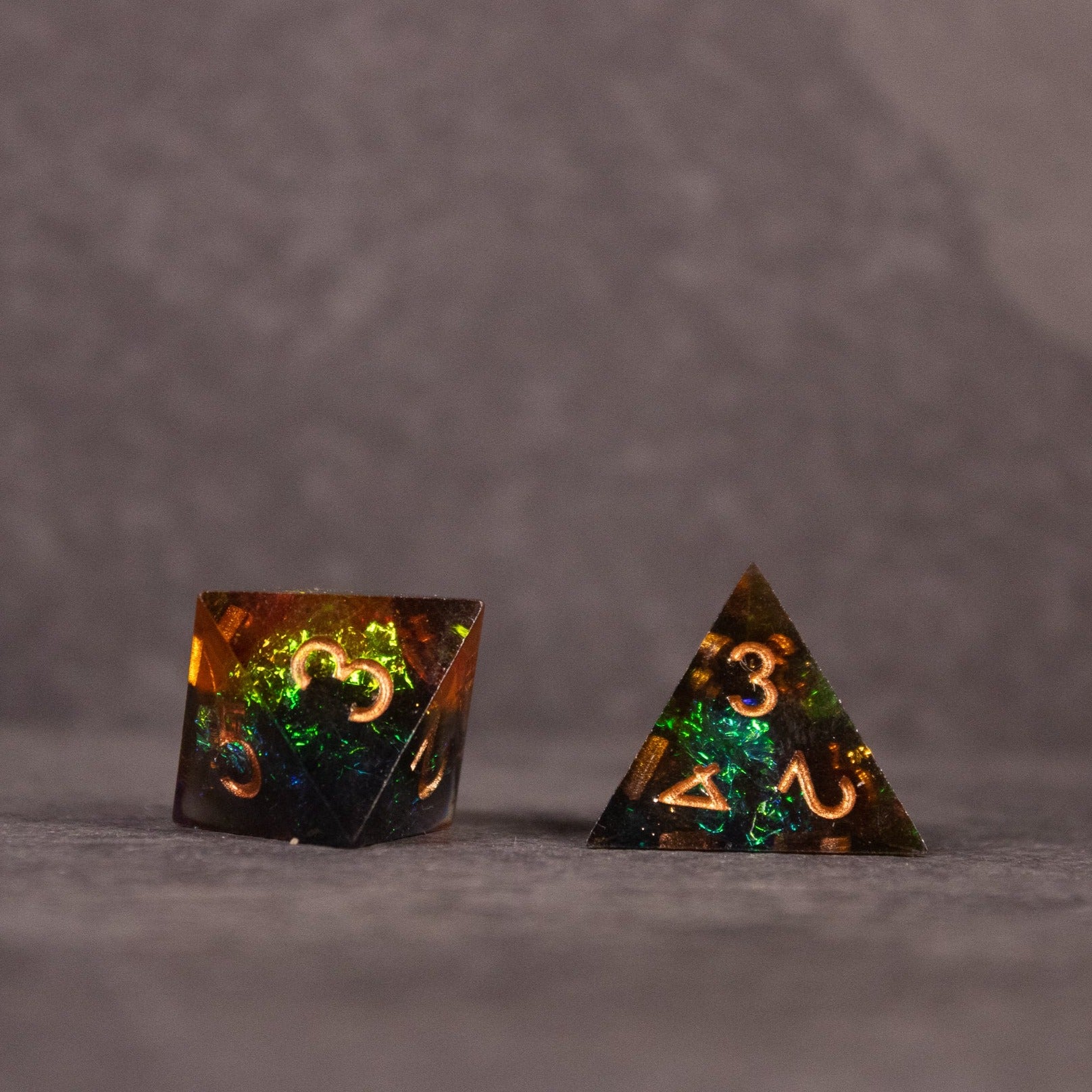 Whiskeyjack Dice Set - Two sharp-edged dice with a translucent amber and dark green swirl and gold numbering, including a d20 and d4.