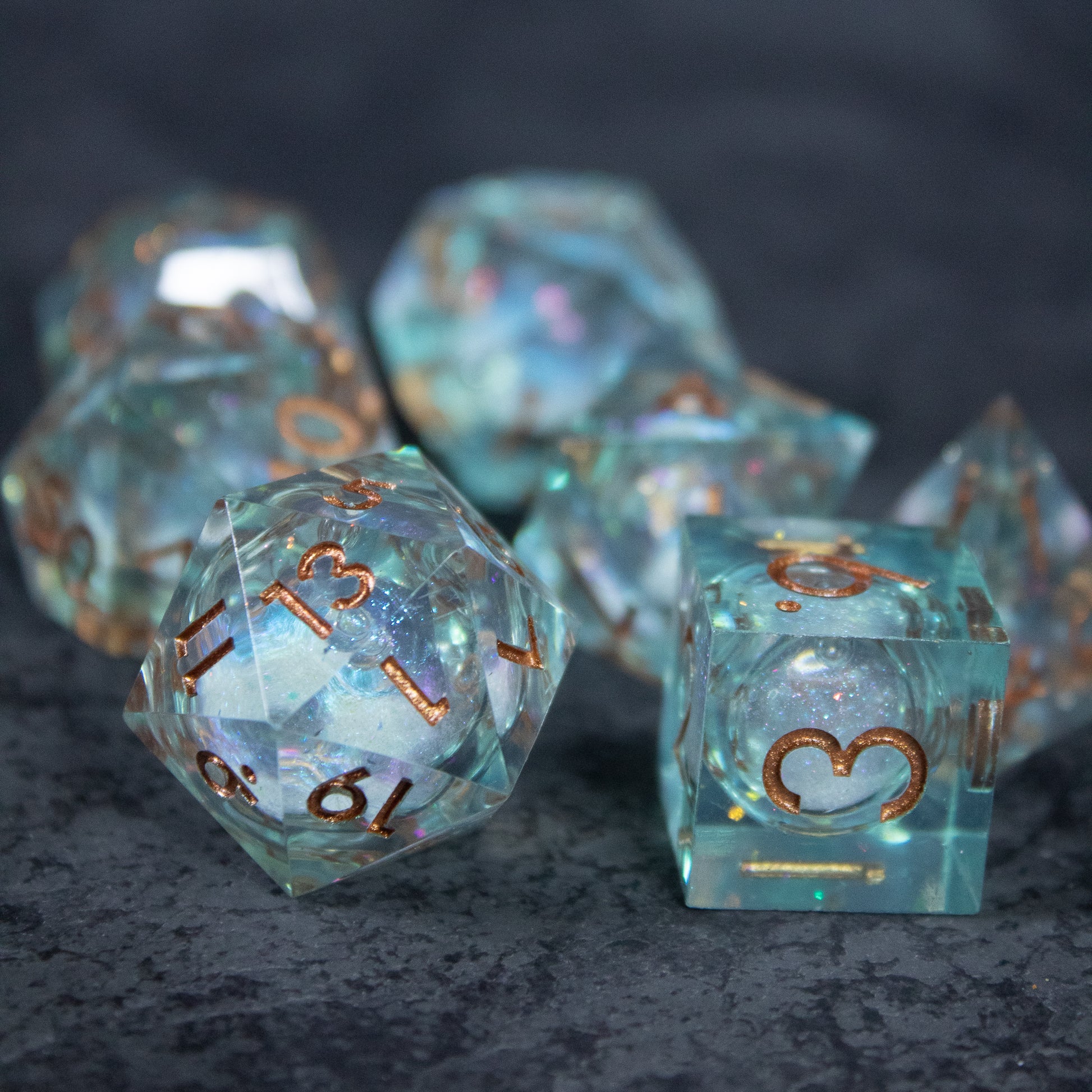 Will o' Wisp Liquid Core Dice Set - Translucent blue-green liquid core polyhedral dice set with sharp edges and metallic copper numbers.