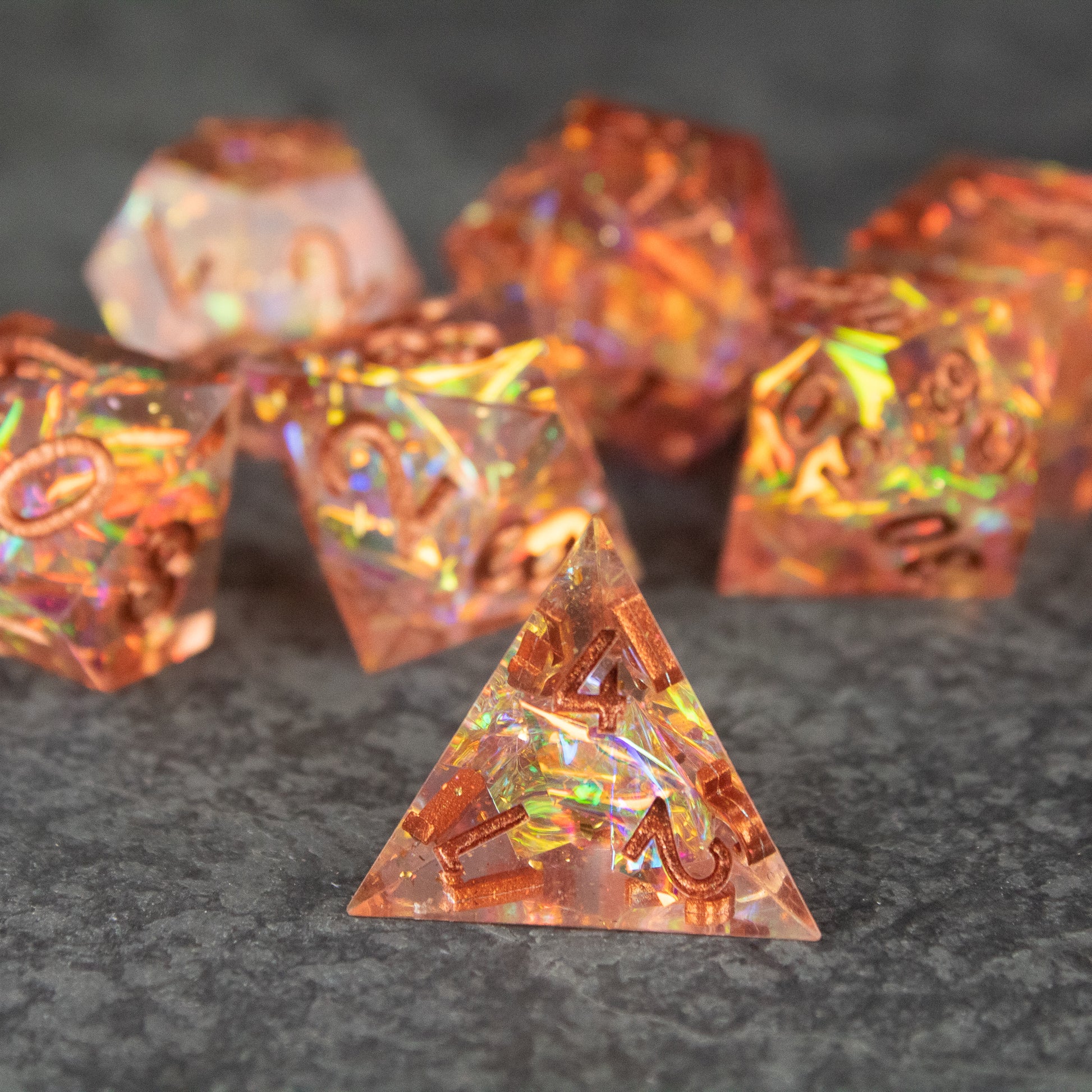 Sacred Flame Dice Set - Orange translucent sharp-edged polyhedral dice with golden numbering and iridescent flame-like inclusions.