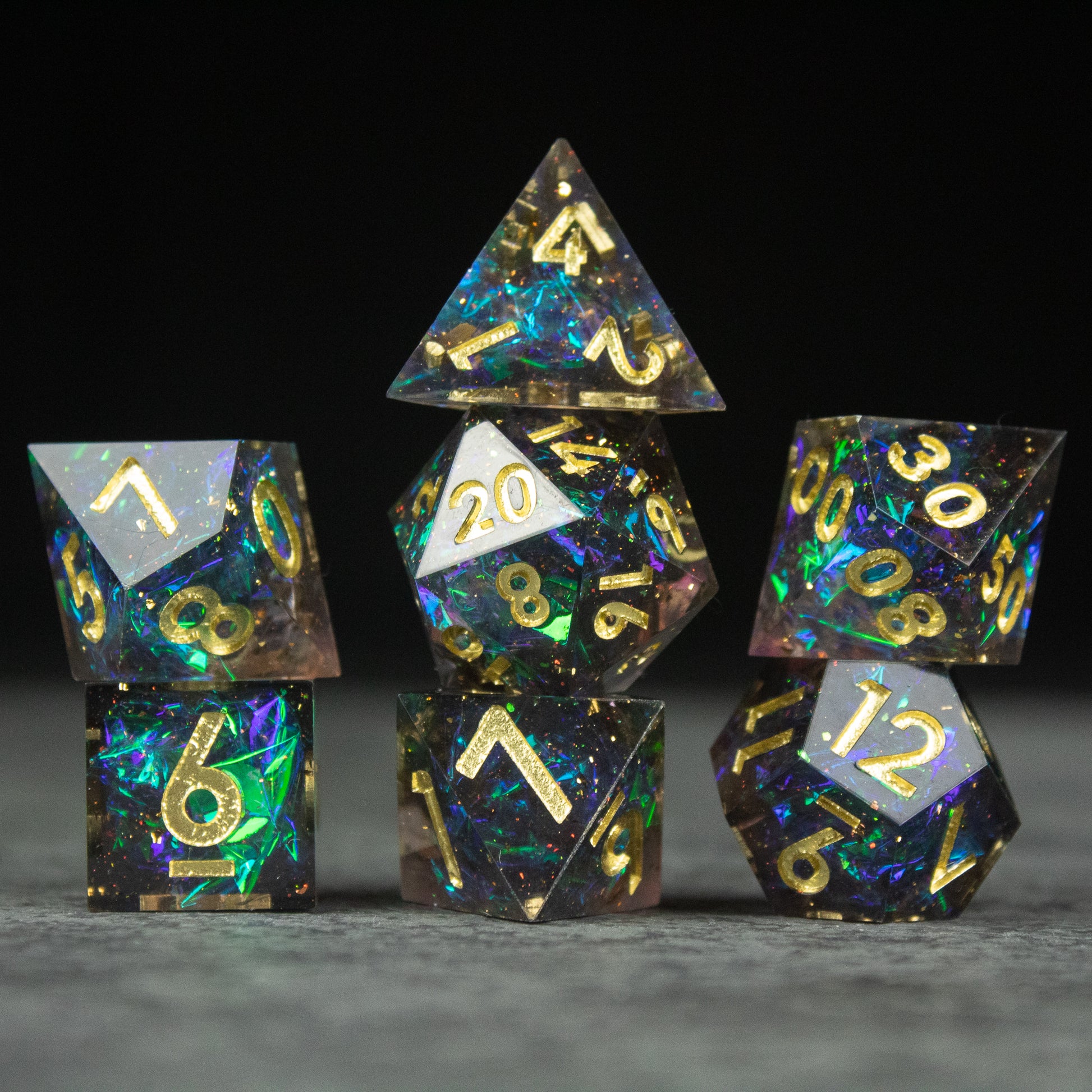 Galaxy Dice Set - Set of seven black sharp-edged dice with iridescent galaxy pattern and gold numbers against dark background.