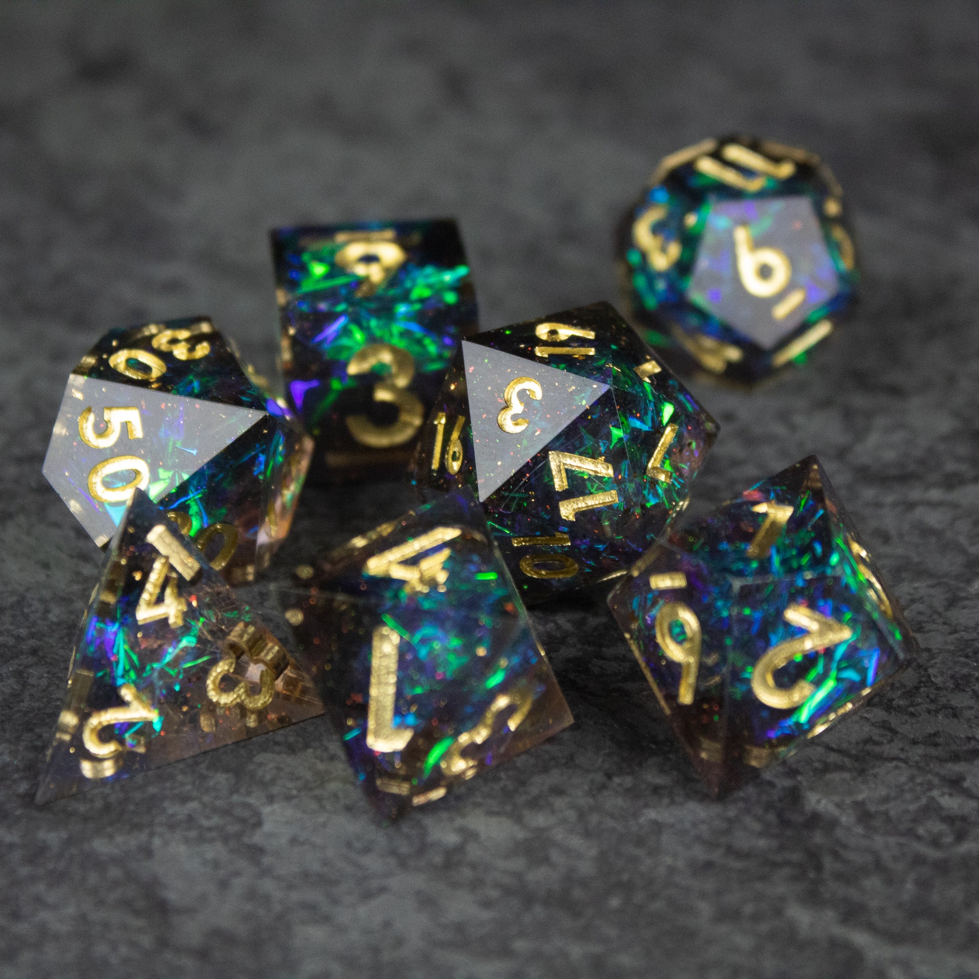 Galaxy Dice Set - Seven black multi-sided dice with sharp edges, embedded with blue and green galaxy-like swirls and gold numbers.