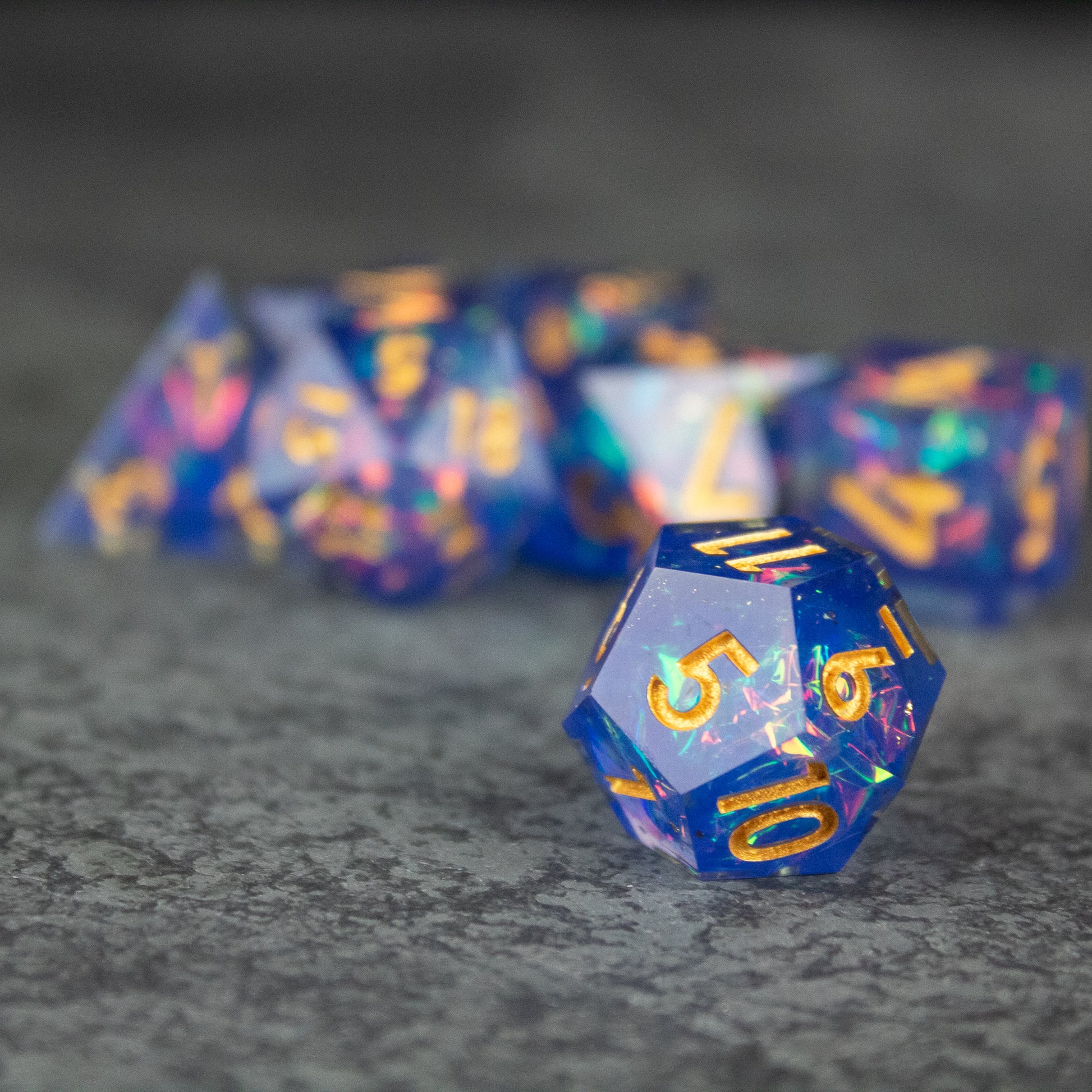 Arcana Dice Set - Translucent blue 20-sided sharp edge die with gold numbers, part of a polyhedral set.