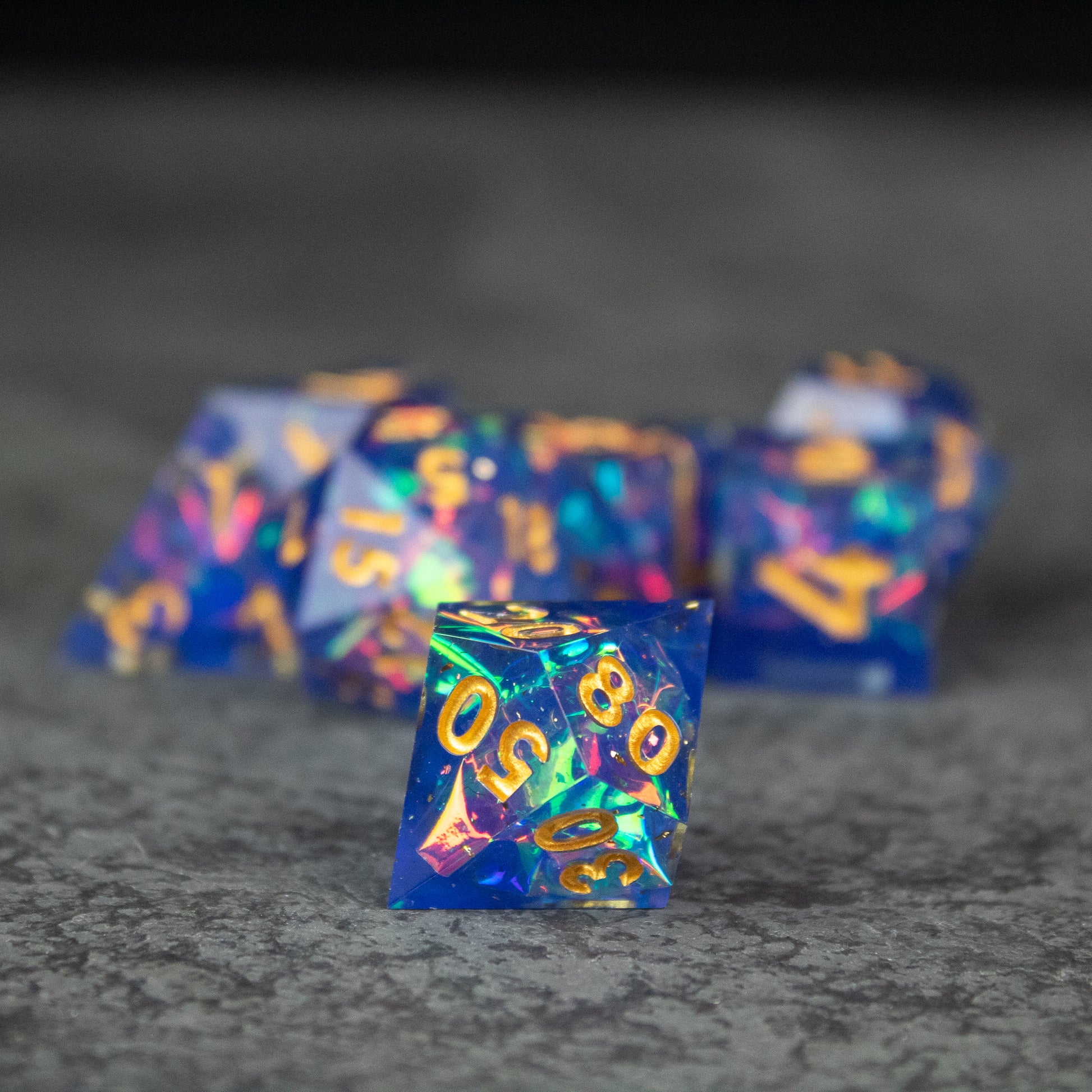 Arcana Dice Set - Set of translucent blue sharp-edged polyhedral dice with gold and colorful numbers.