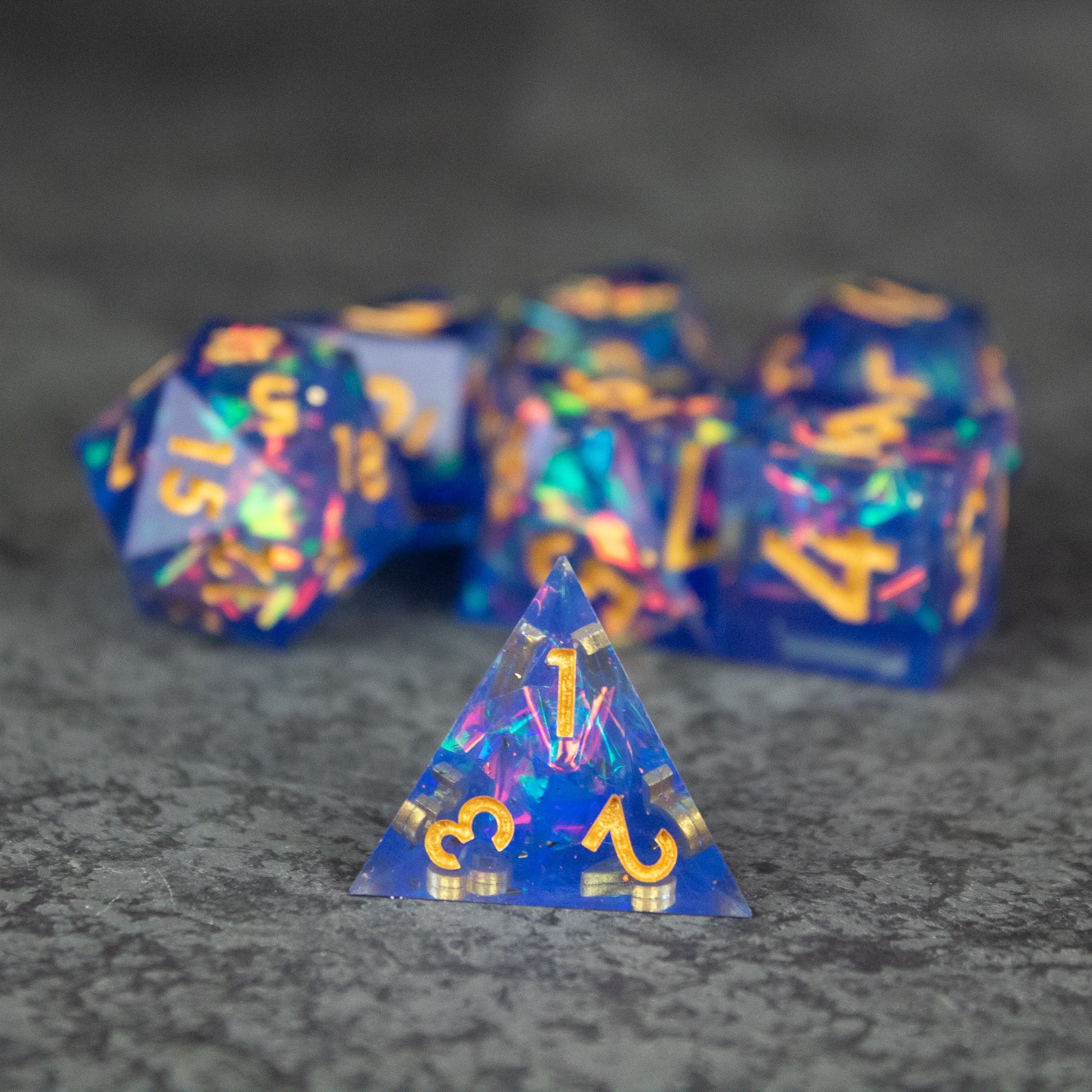 Arcana Dice Set - Set of translucent blue sharp-edged polyhedral dice with gold numbers, featuring a pyramid-shaped d4 die in front.