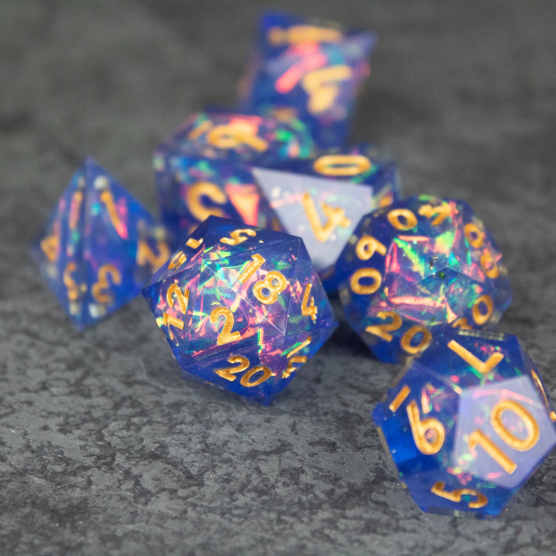 Arcana Dice Set - Blue sharp-edged polyhedral dice set with gold numbers and iridescent multicolor flakes.
