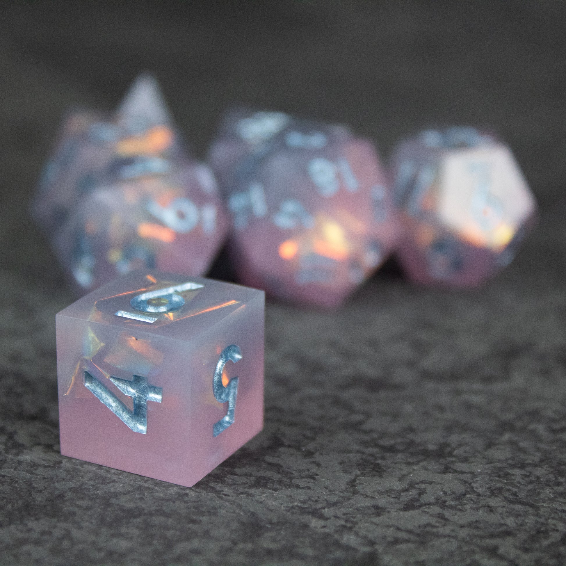 Moonshard Dice Set - Translucent pink sharp-edged dice with metallic silver numbers, including a prominent six-sided die in front.