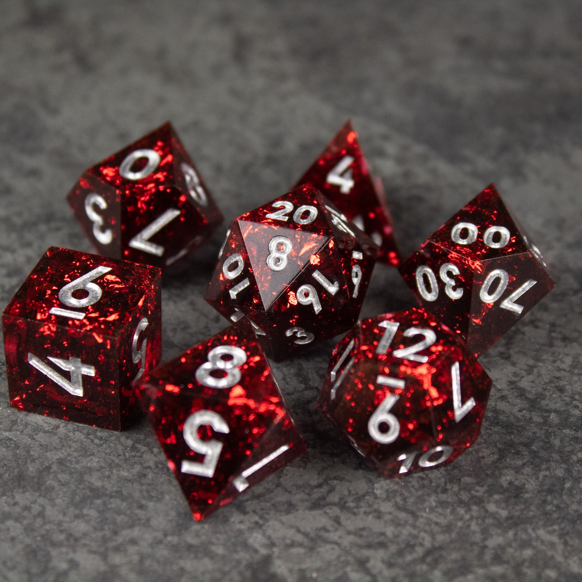 Inferno Dice Set - Set of seven translucent red sharp-edged dice with white numbers on a gray surface.
