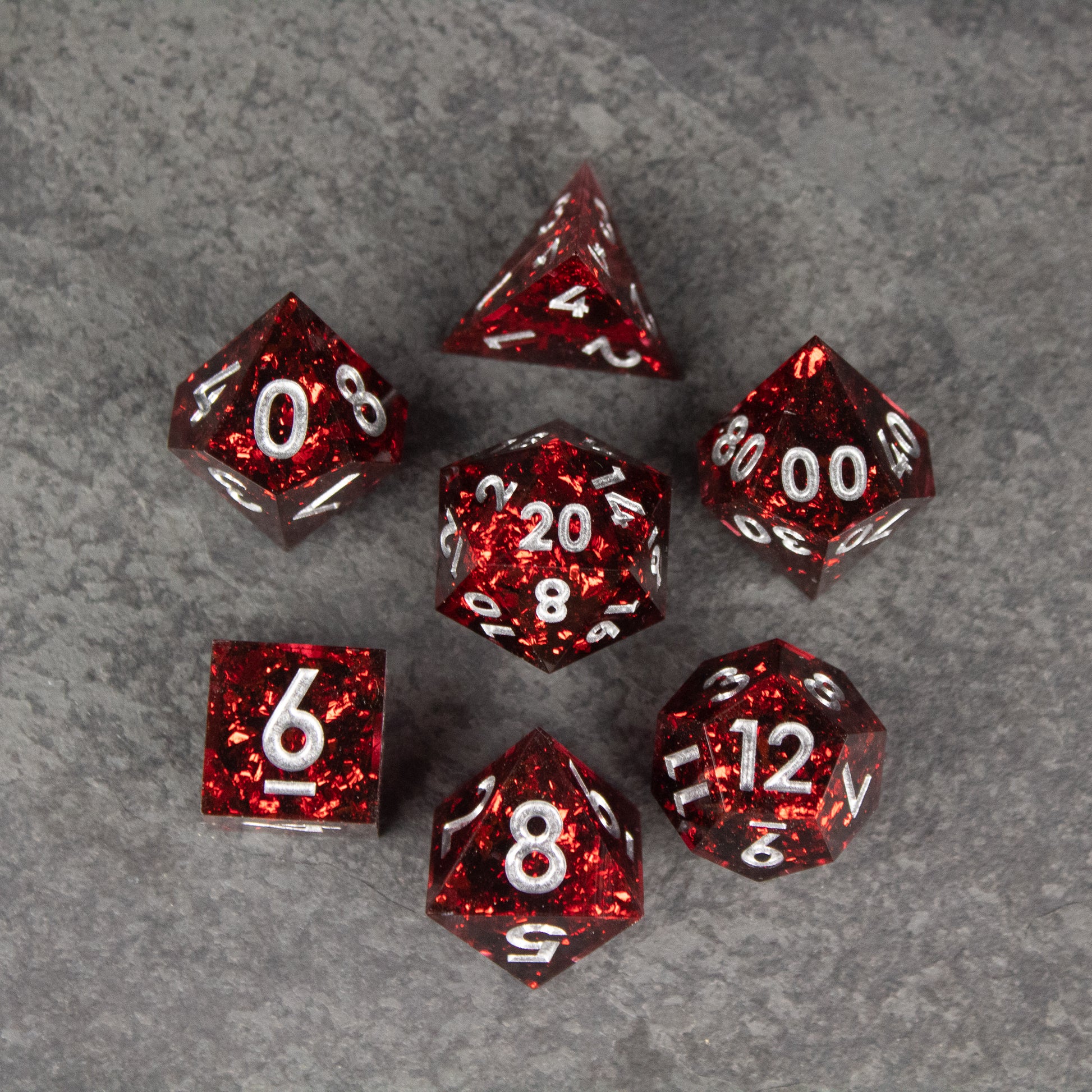 Inferno Dice Set - Set of seven translucent red sharp-edged dice with white numbering on gray surface.