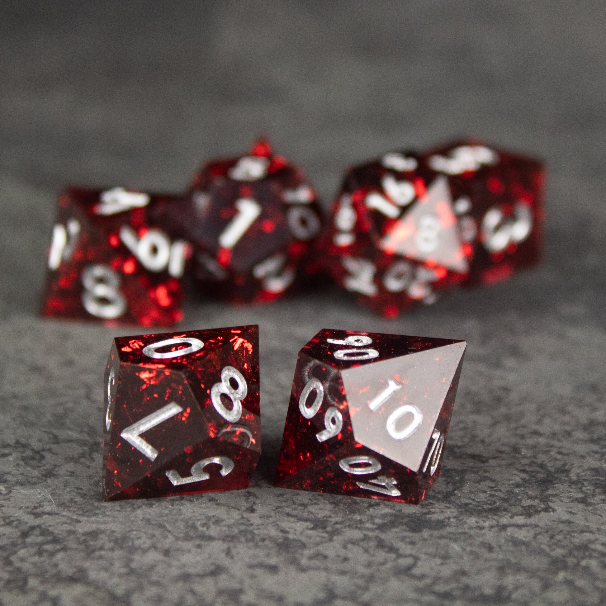Inferno Dice Set - Red translucent polyhedral dice set with sharp edges and white numbering on gray surface.
