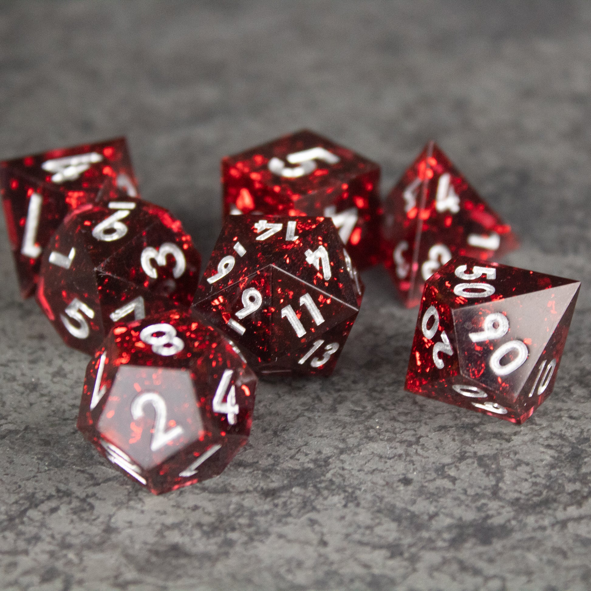 Inferno Dice Set - Set of seven translucent red polyhedral dice with sharp edges and white numbering on a gray textured surface.