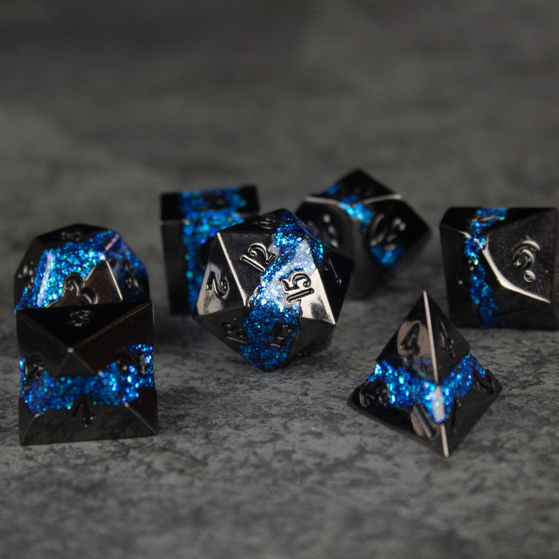 Blue Rift Dice Set - Metallic black and blue seven-piece tabletop RPG dice set with silver numbers on a gray surface.