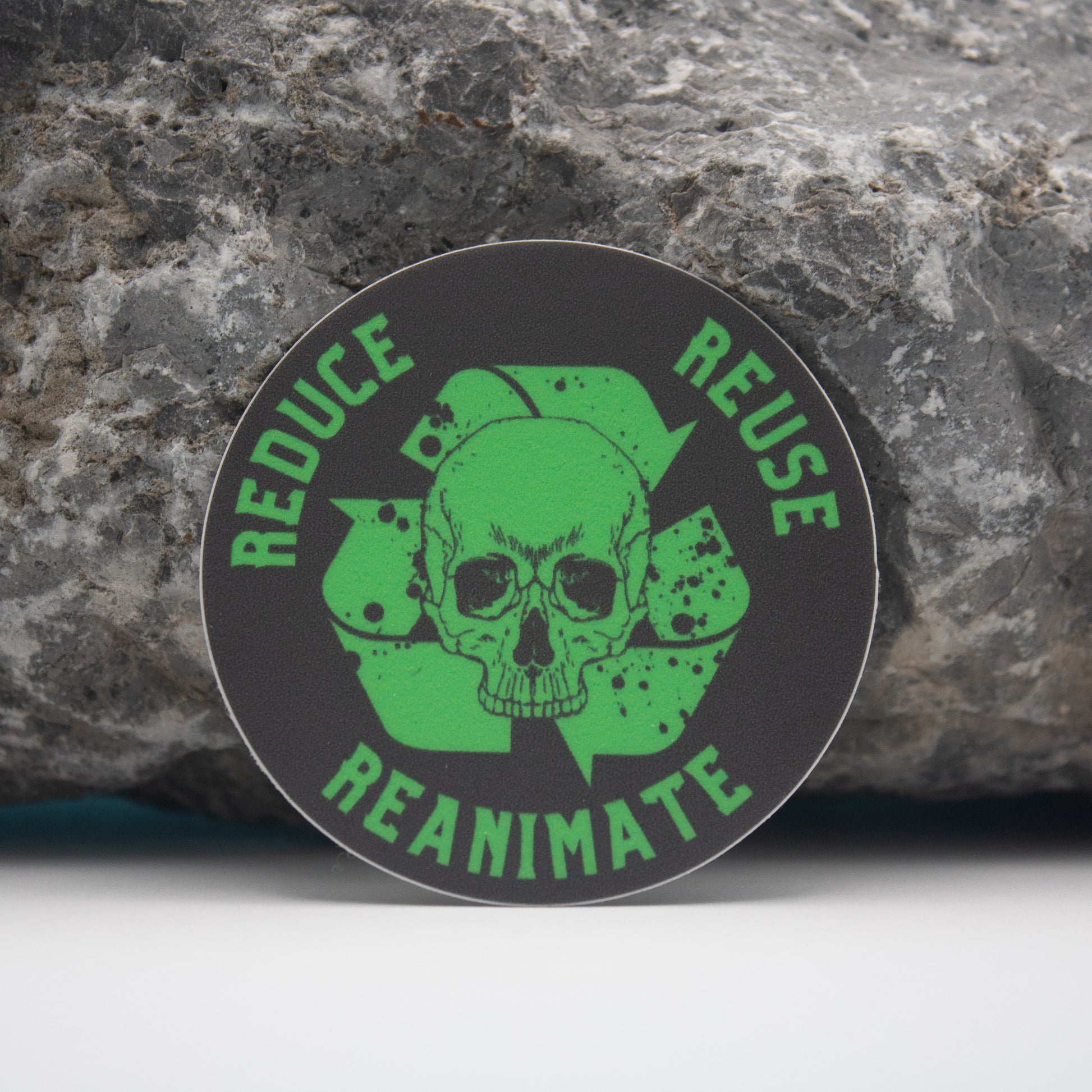 Reduce, Reuse, Reanimate DnD Sticker - Round sticker with green skull and crossbones over a clover, text "Reduce Reuse Reanimate" on black background.