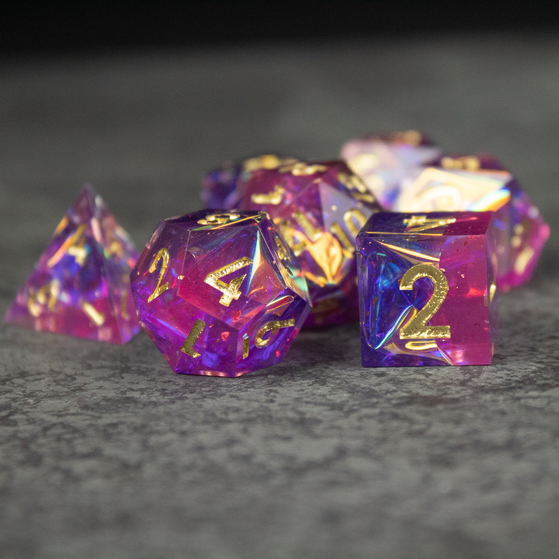 Aether Dice Set - Set of translucent sharp-edged dice in vibrant pink and purple with gold numbers.