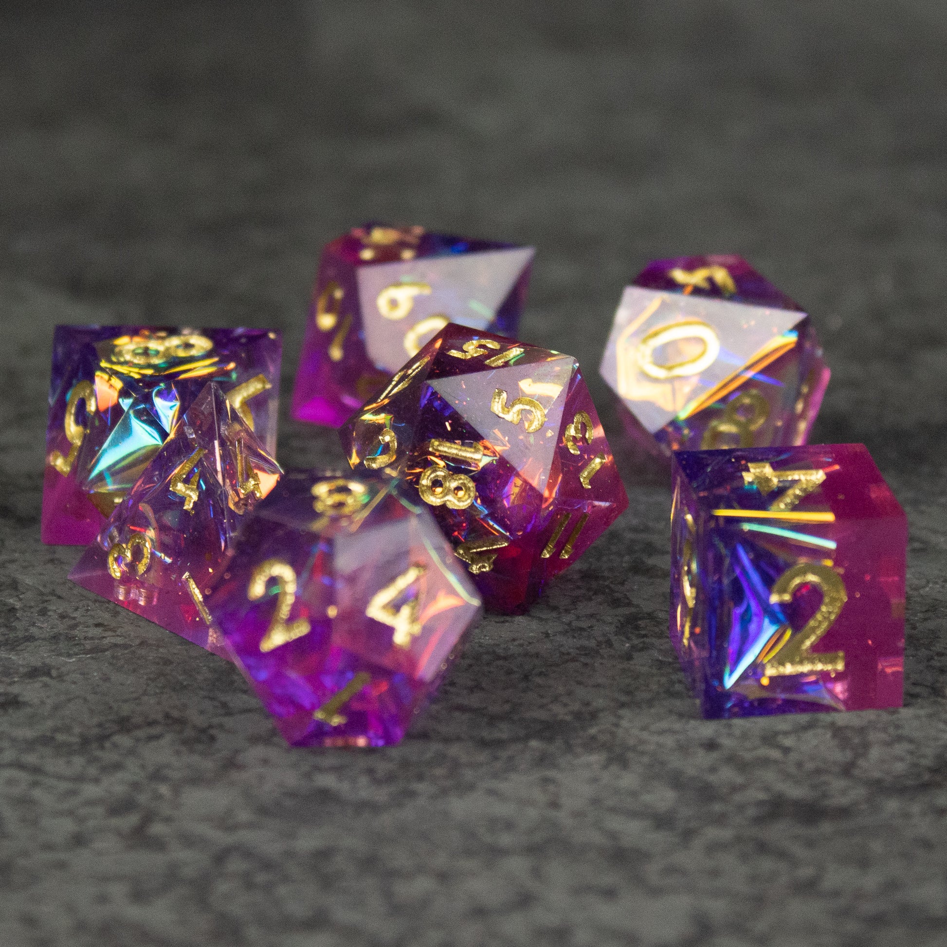 Aether Dice Set - Set of seven translucent sharp-edged dice blending pink and purple with gold numbers on each face.