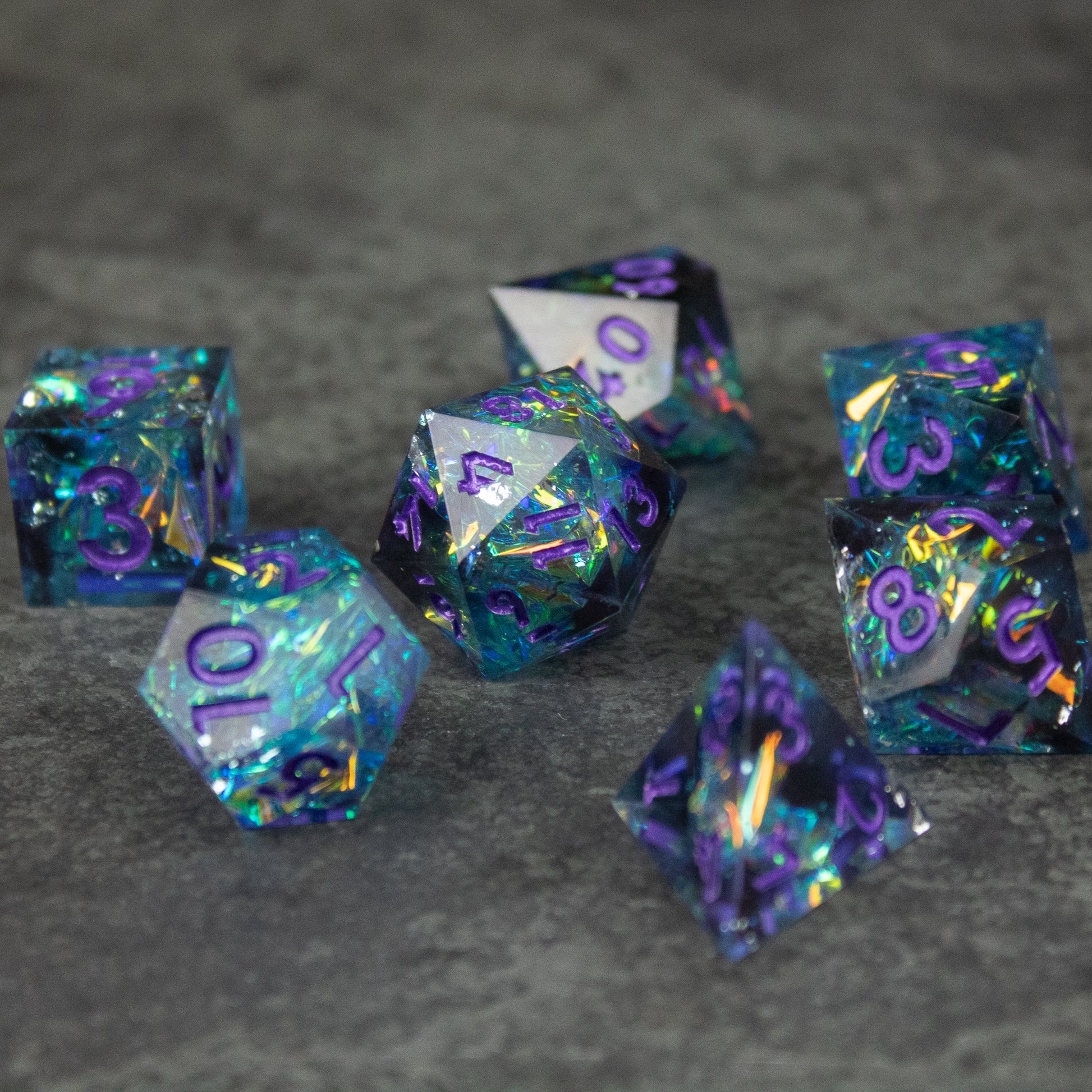 Frostbite Dice Set - Seven sharp-edged 20-sided dice in translucent blue and black with iridescent shimmer and purple numbering.