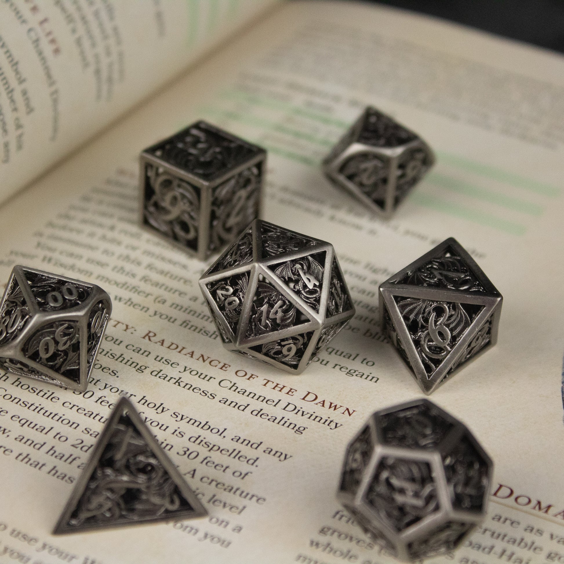 Dragon Cult Hollow Dice Set - Set of black hollow metal polyhedral dice with intricate dragon and geometric engravings.