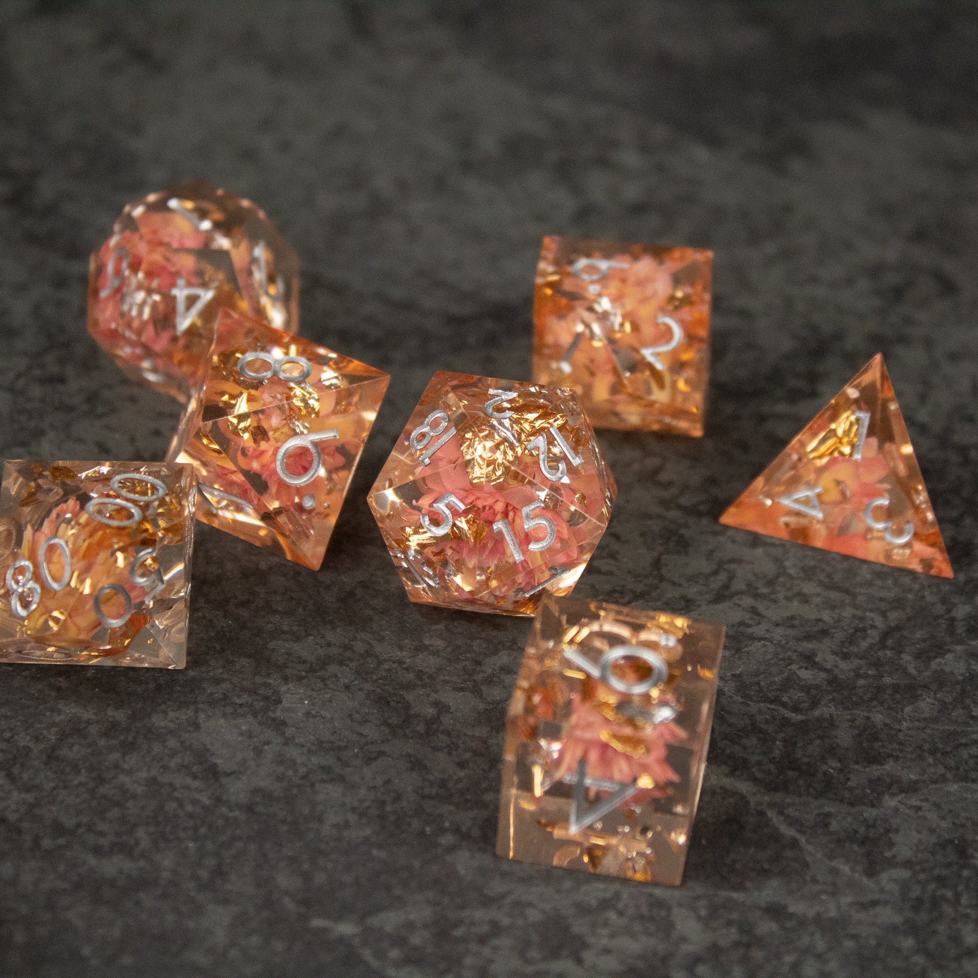 Pink Flower Sharp Edge Dice Set - Set of seven sharp-edged translucent pink dice with embedded flower petals and white numbering.