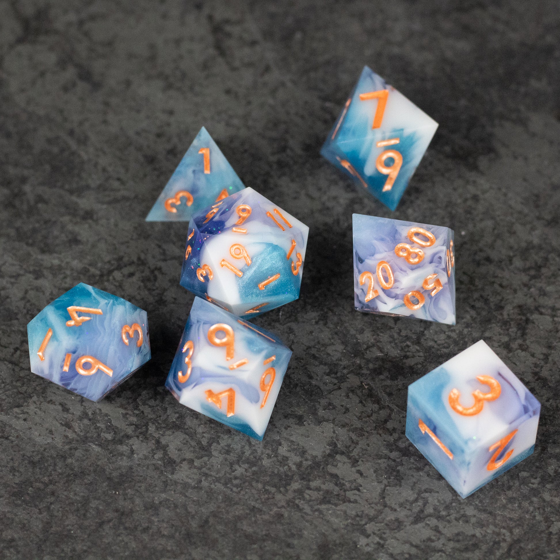 Cloudscape Dice Set - Seven blue and white marbled sharp-edged dice with orange numbers on dark textured surface.