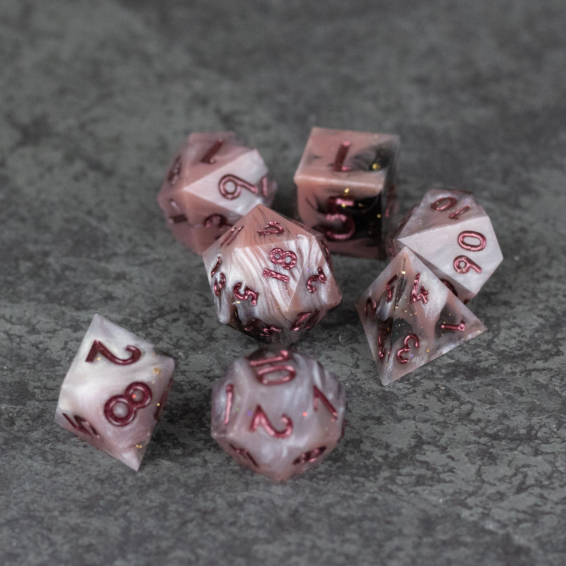 Rosestone Dice Set - Seven polyhedral dice in translucent red with sharp edges and gold numbering on a gray textured surface.