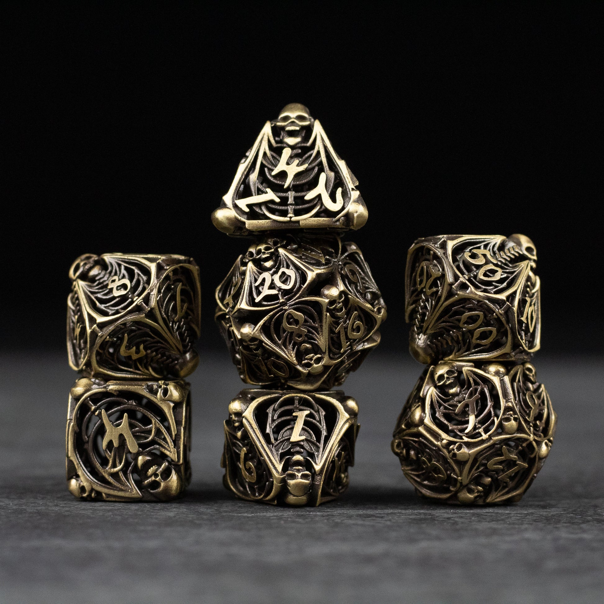 Bone Crypt Dice Set - Set of seven hollow metal dice in black and gold with intricate bone and crypt-inspired designs.