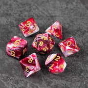 Red and White Marbled Dice Set - Set of seven acrylic dice with red and white marbled patterns and gold numbering on a dark surface.