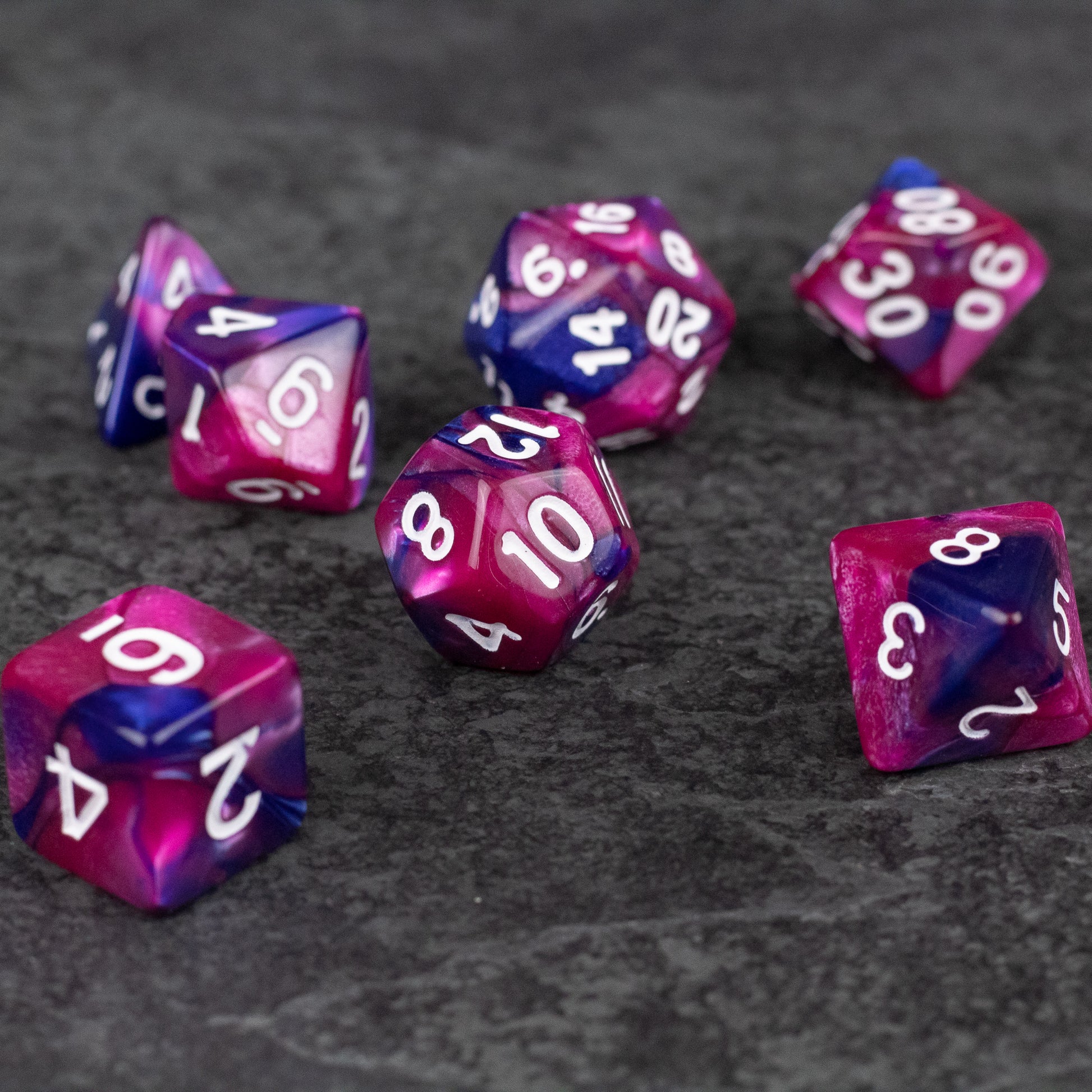 Pink and Blue Marbled Dice Set - Set of pink and blue marbled acrylic dice with white numbering, various polyhedral shapes on dark surface.