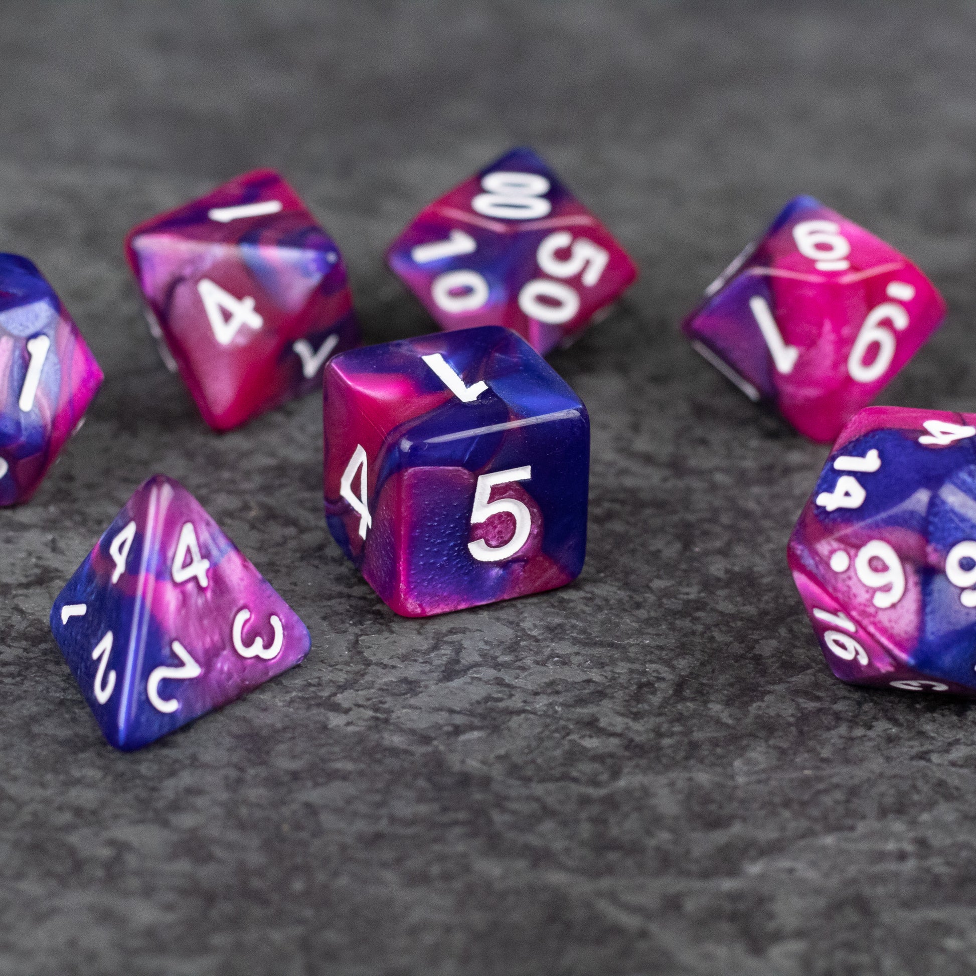 Pink and Blue Marbled Dice Set - Set of seven acrylic dice in swirled pink and blue marbled patterns with white numbers, including varied polyhedral shapes.