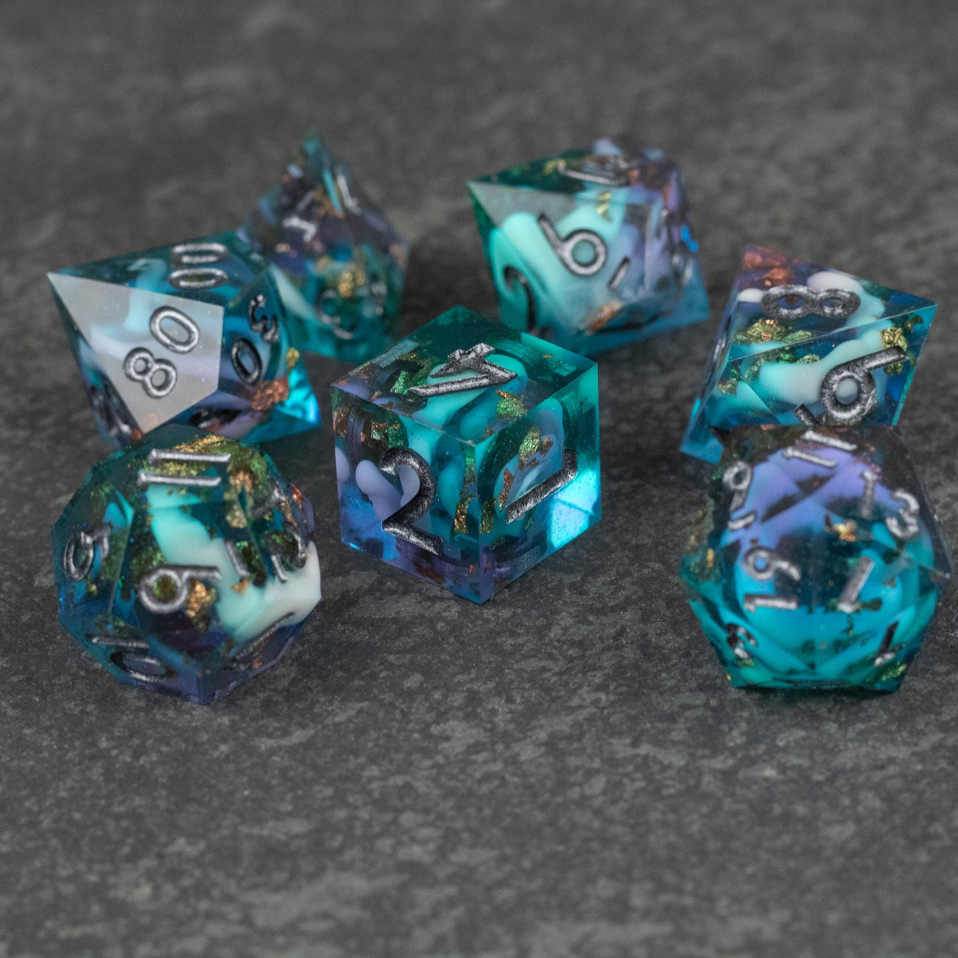 Frostfall Dice Set - Set of seven polyhedral dice with sharp edges in swirling blue, teal, and purple colors with metallic gold numbers.