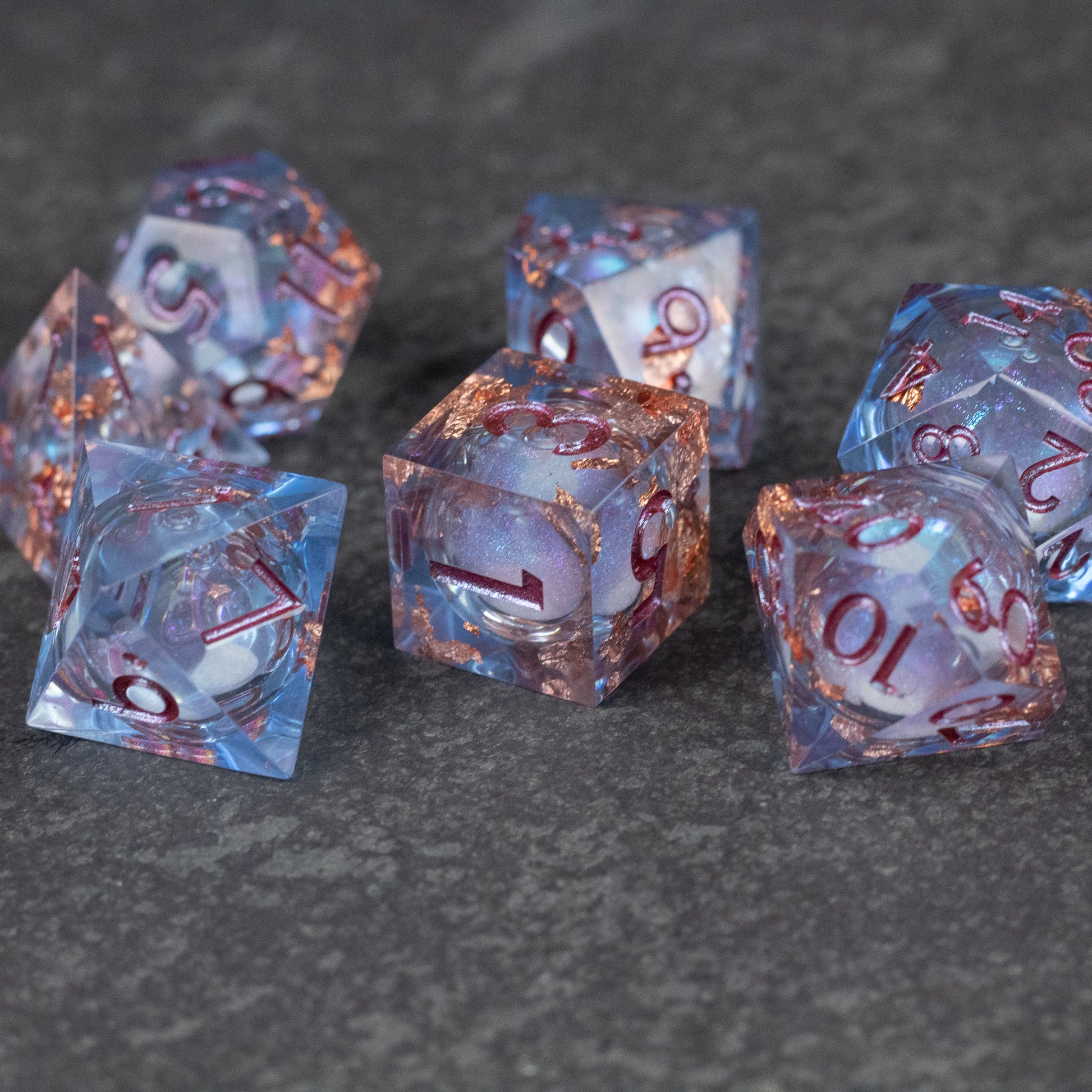 Temporal Rift Liquid Core Dice Set - Set of seven translucent blue polyhedral dice with sharp edges and swirling liquid core, red numbering.