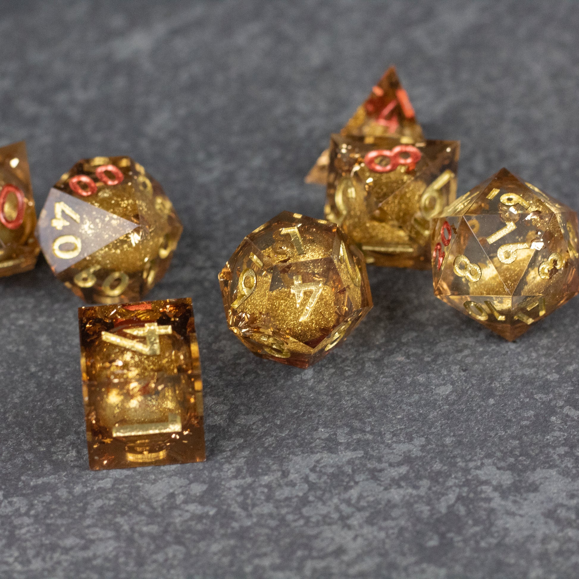 Dragon's Hoard Liquid Core Dice Set - Set of seven translucent gold polyhedral dice with sharp edges and gold numbers on a dark textured surface.