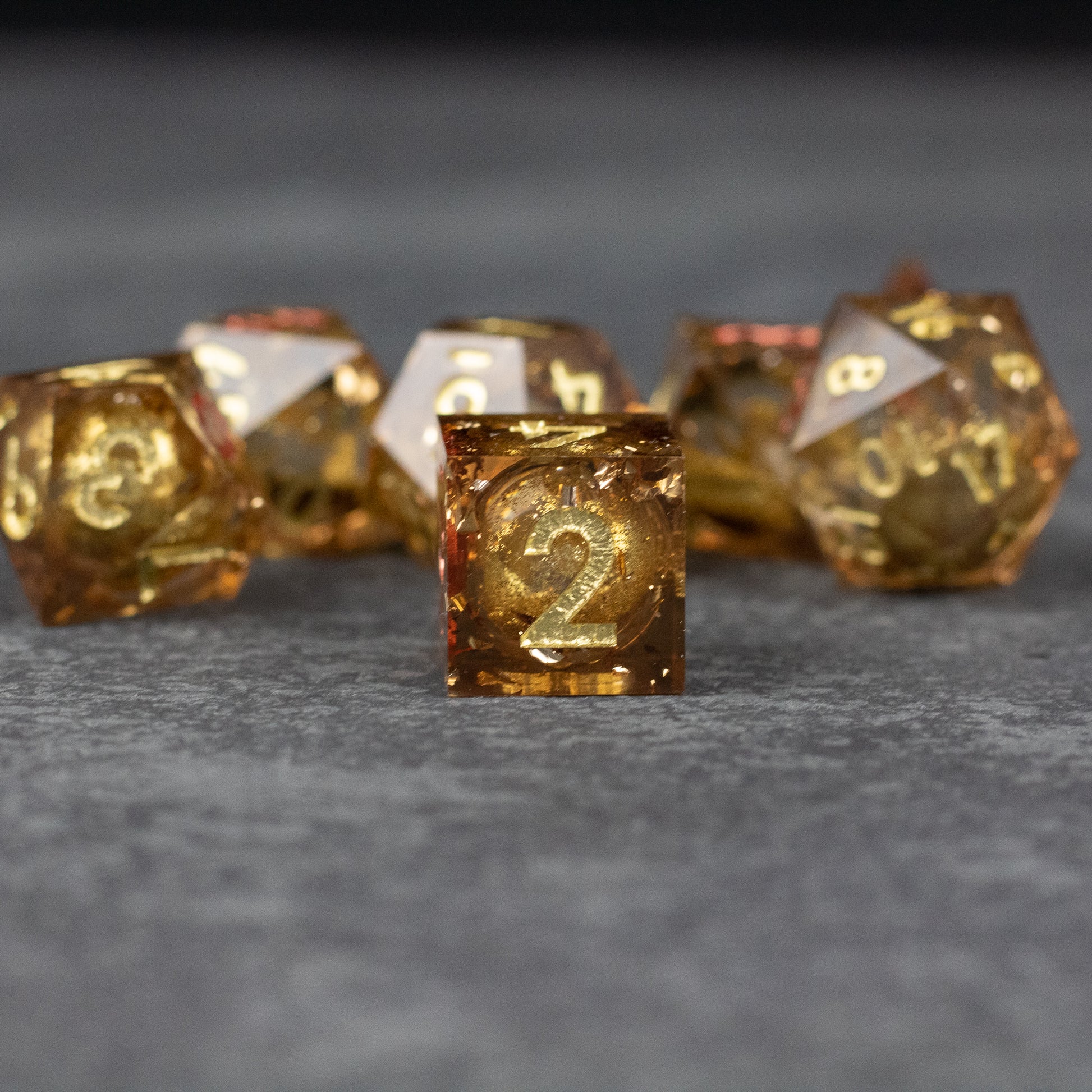 Dragon's Hoard Liquid Core Dice Set - Gold sharp-edged dice with liquid core and glittery inclusions, featuring a prominent number 2 on the central die.