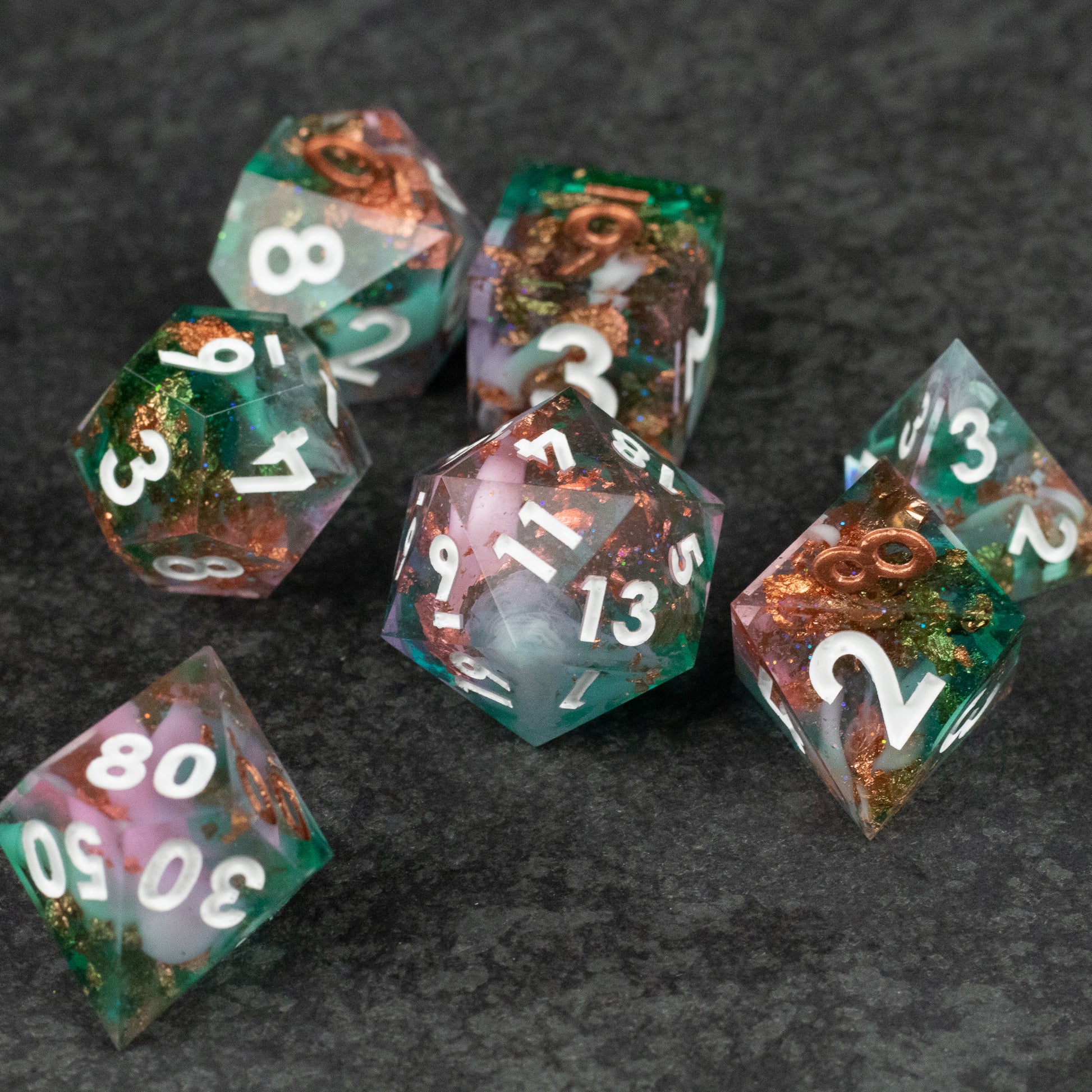 Scapeshift Dice Set - Set of seven translucent sharp-edged dice with green, pink, and copper metallic swirls and white numbers.