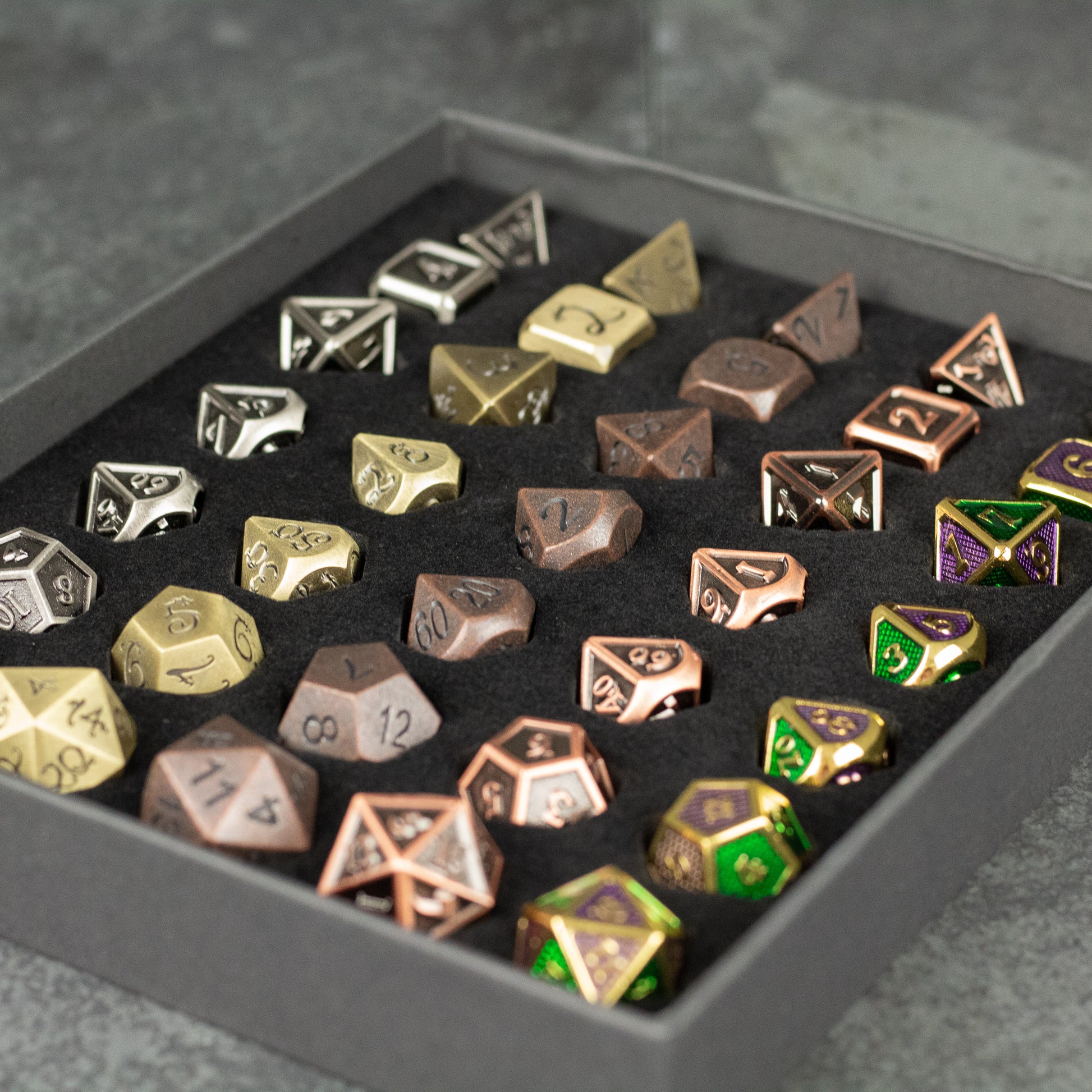 Metal Dice Set Gift Box - Set of metal polyhedral dice in silver, gold, bronze, and green with gold numbers, displayed in a black gift box with foam.