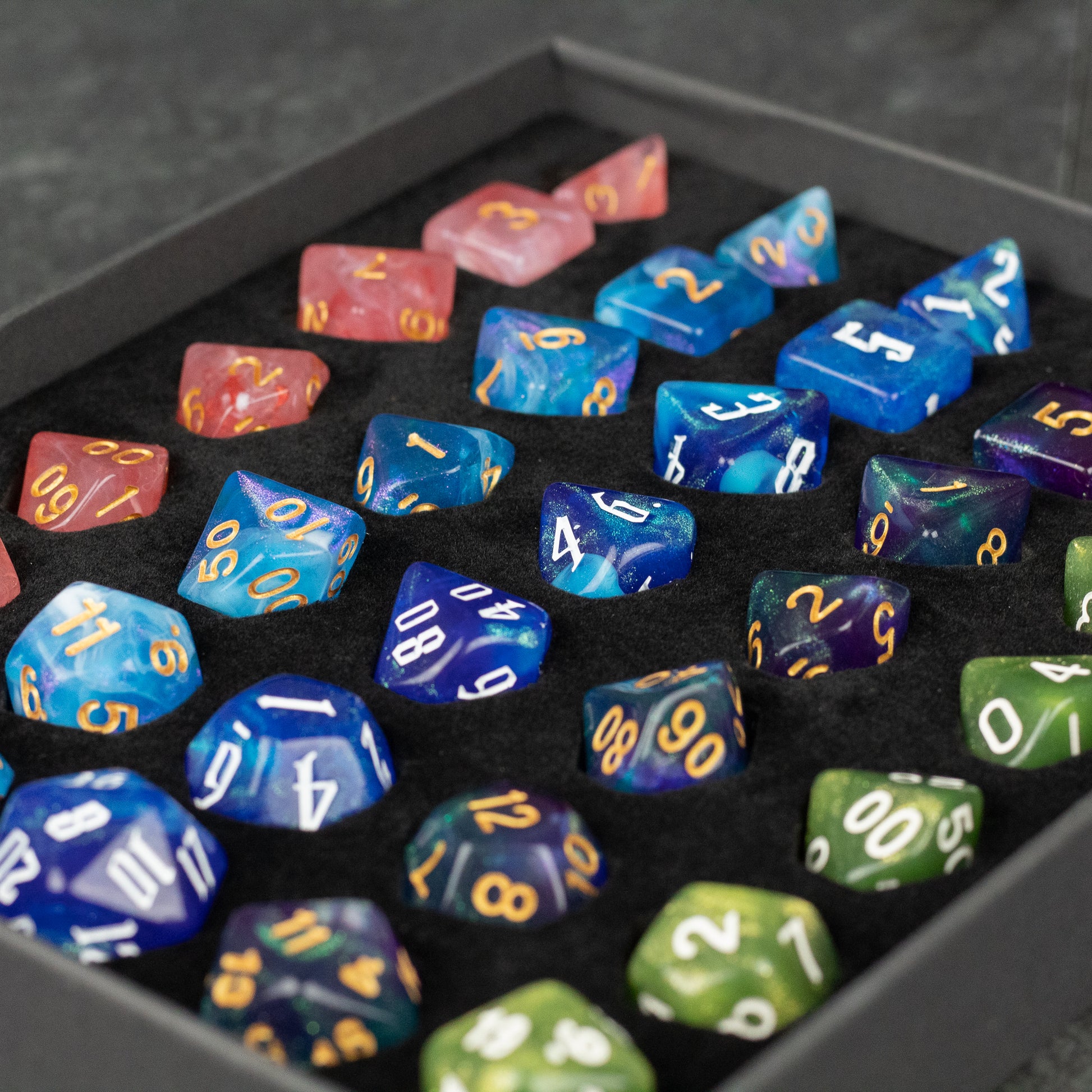Acrylic Dice Set Gift Box - Set of colorful translucent acrylic polyhedral dice in blue, green, purple, and orange with gold and white numbering,.