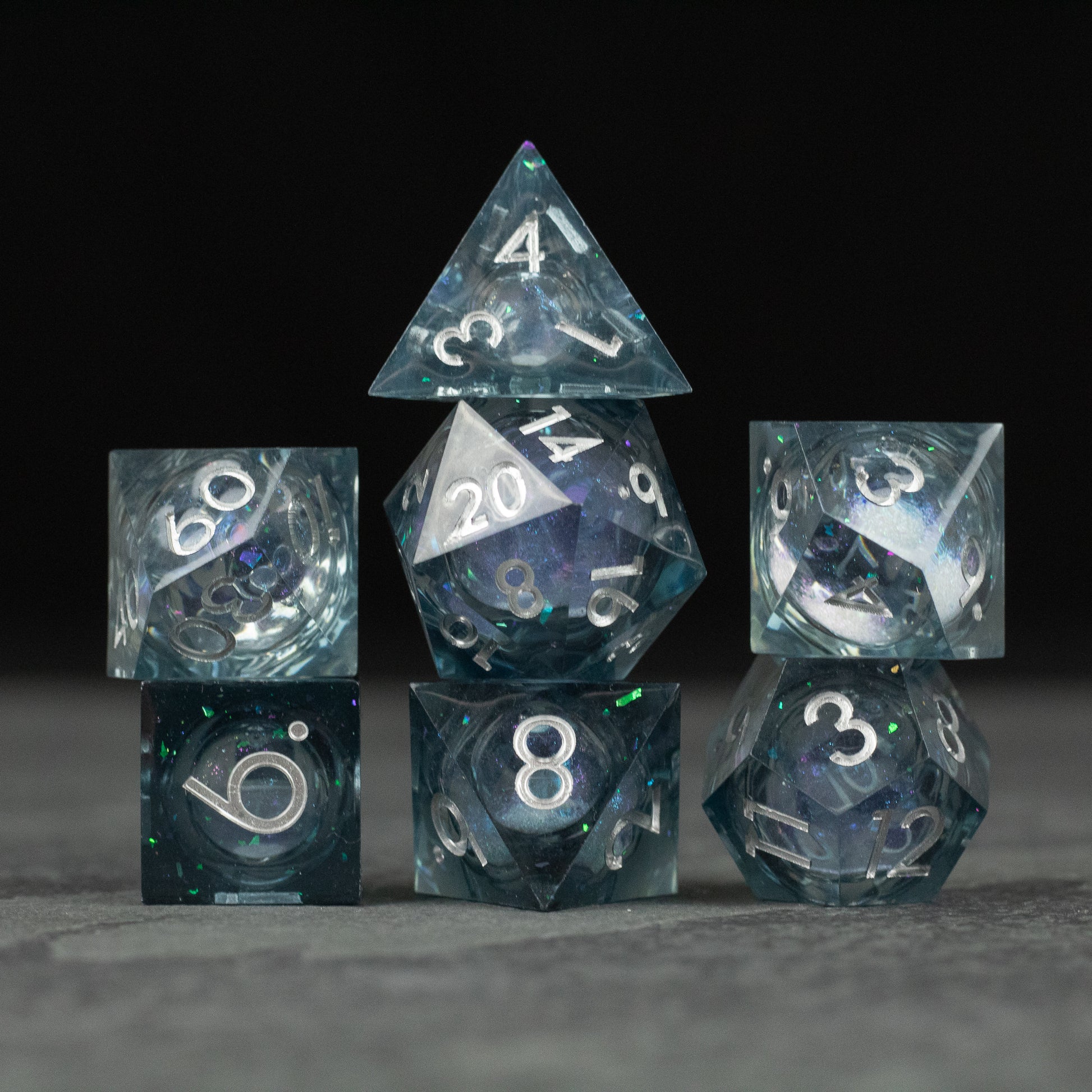 Astral Sea Liquid Core Dice Set - Set of seven transparent polyhedral dice with sharp edges, containing swirling blue and white liquid core and white.