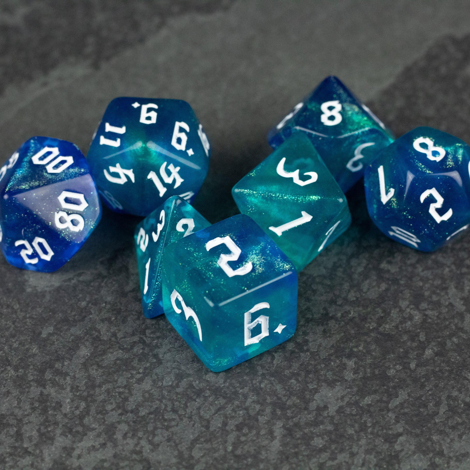 Blue & Green Glitter Dice Set - Set of translucent blue and green glitter polyhedral dice with white numbers on a gray surface.