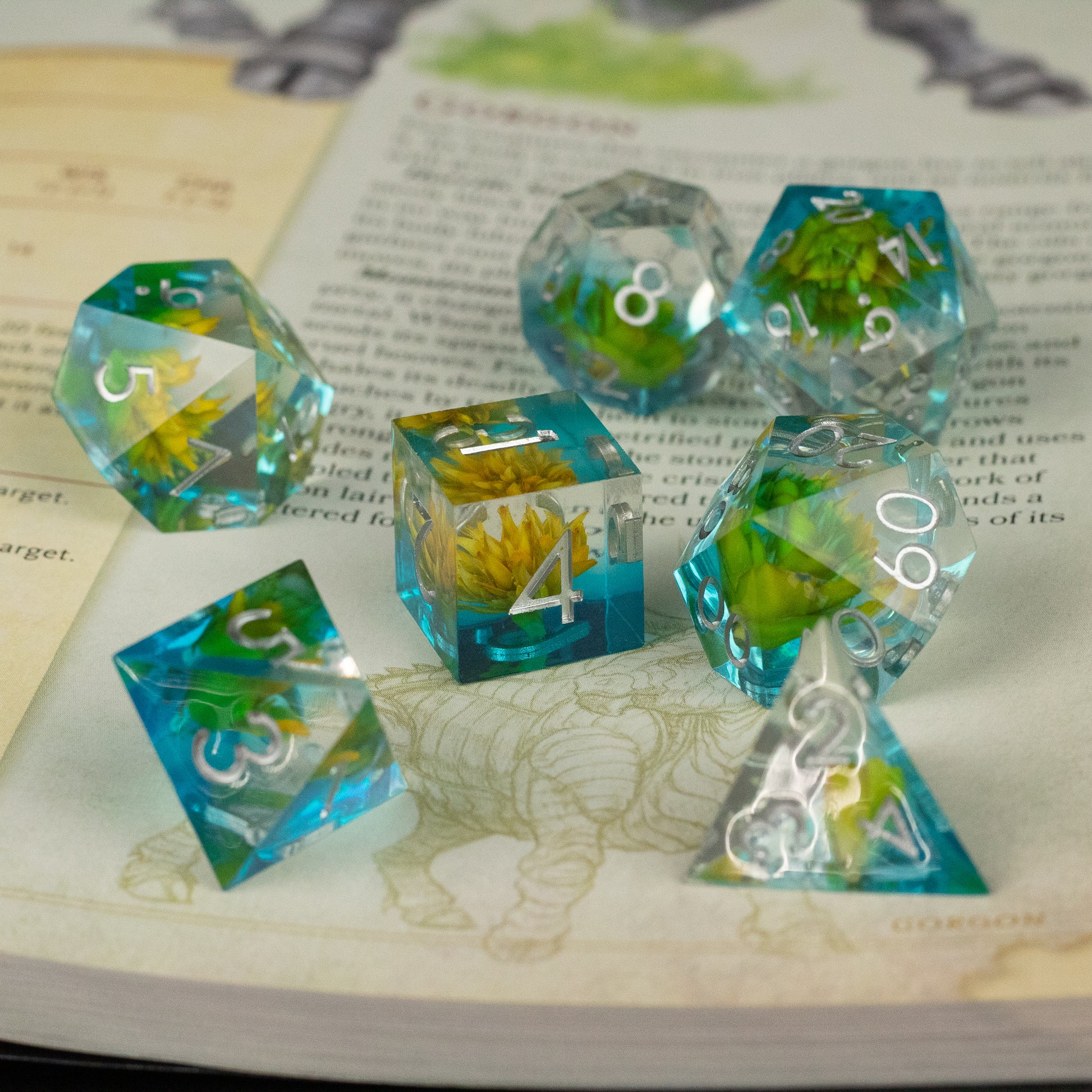 Yellow Flower + Blue Resin Sharp Edge Dice Set - Set of sharp edge polyhedral dice with clear blue resin and embedded yellow flowers, white numbering.