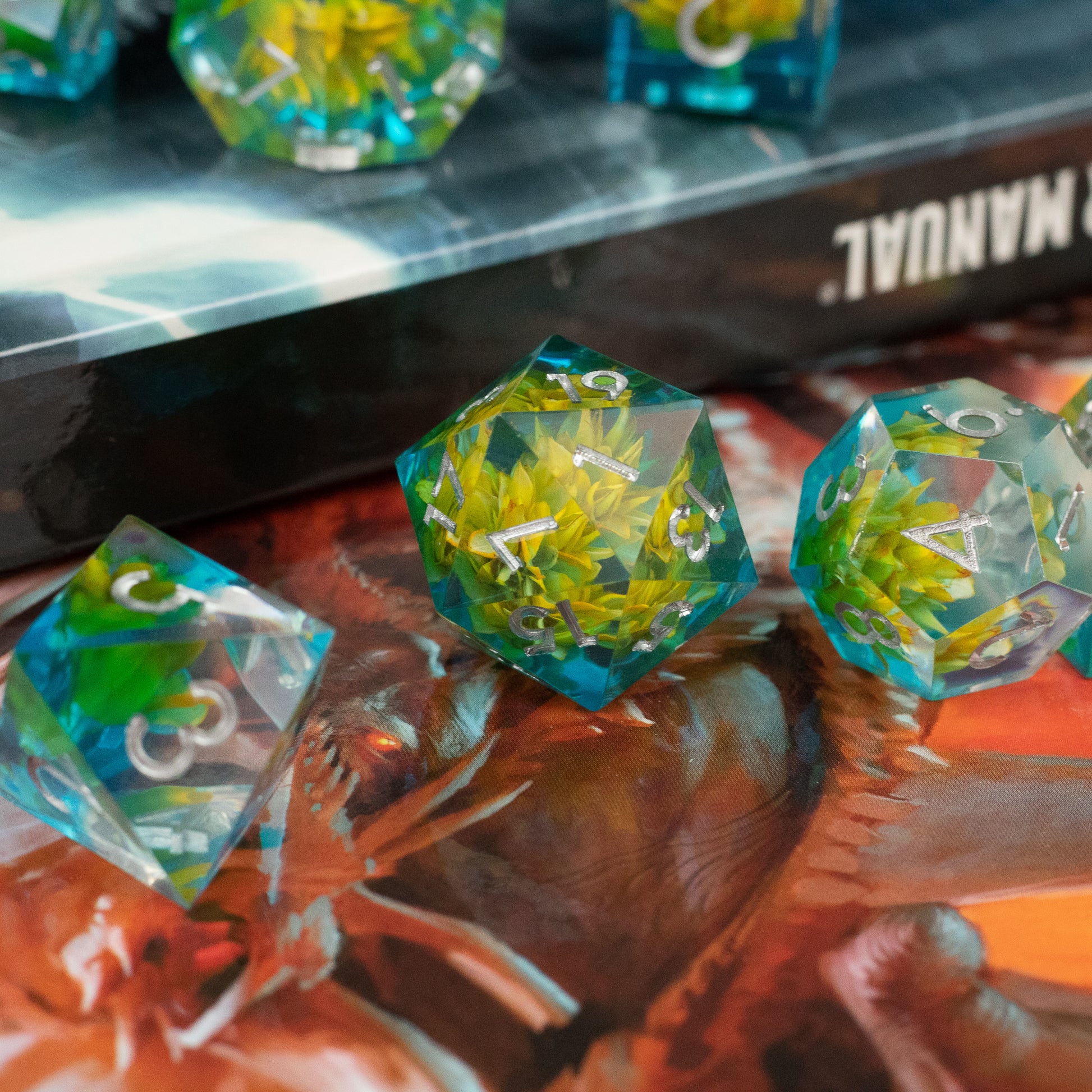 Yellow Flower + Blue Resin Sharp Edge Dice Set - Set of translucent blue sharp-edged dice with embedded yellow flowers and green foliage details.