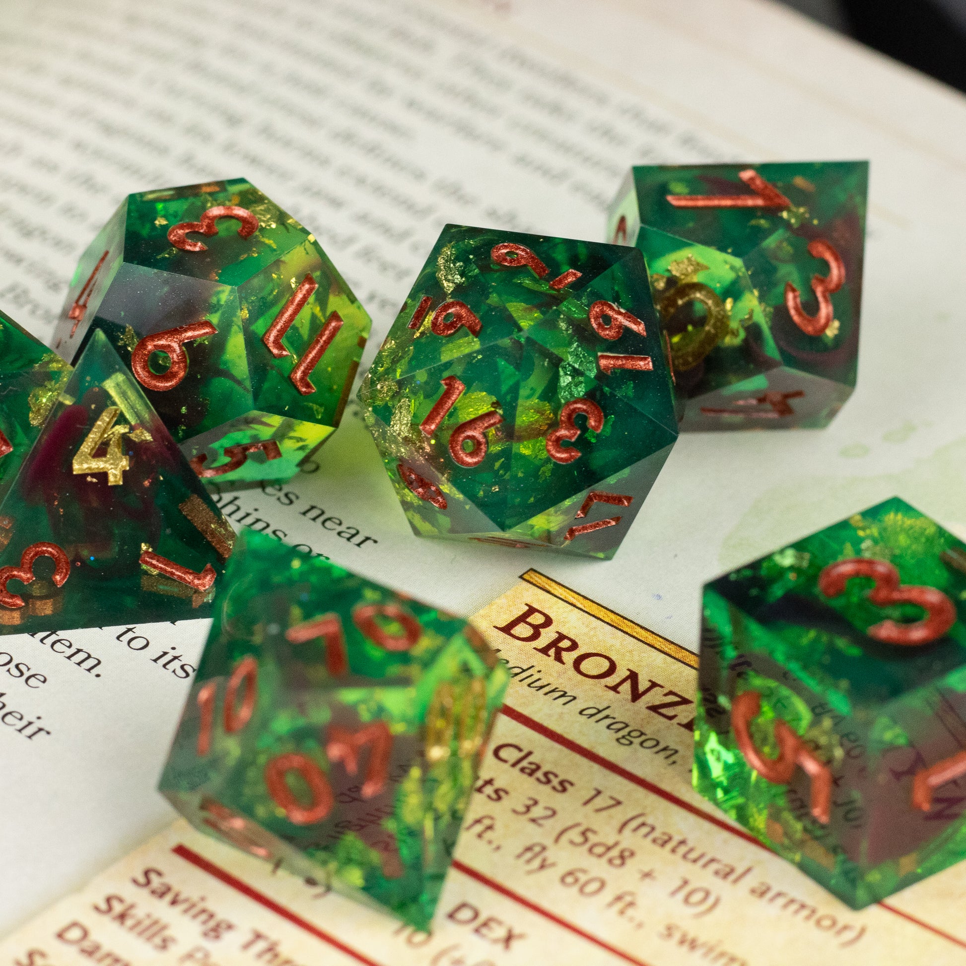 Primal Blood Dice Set - Green transparent polyhedral dice set with sharp edges and red metallic numbers, including a 20-sided die, resting on book.