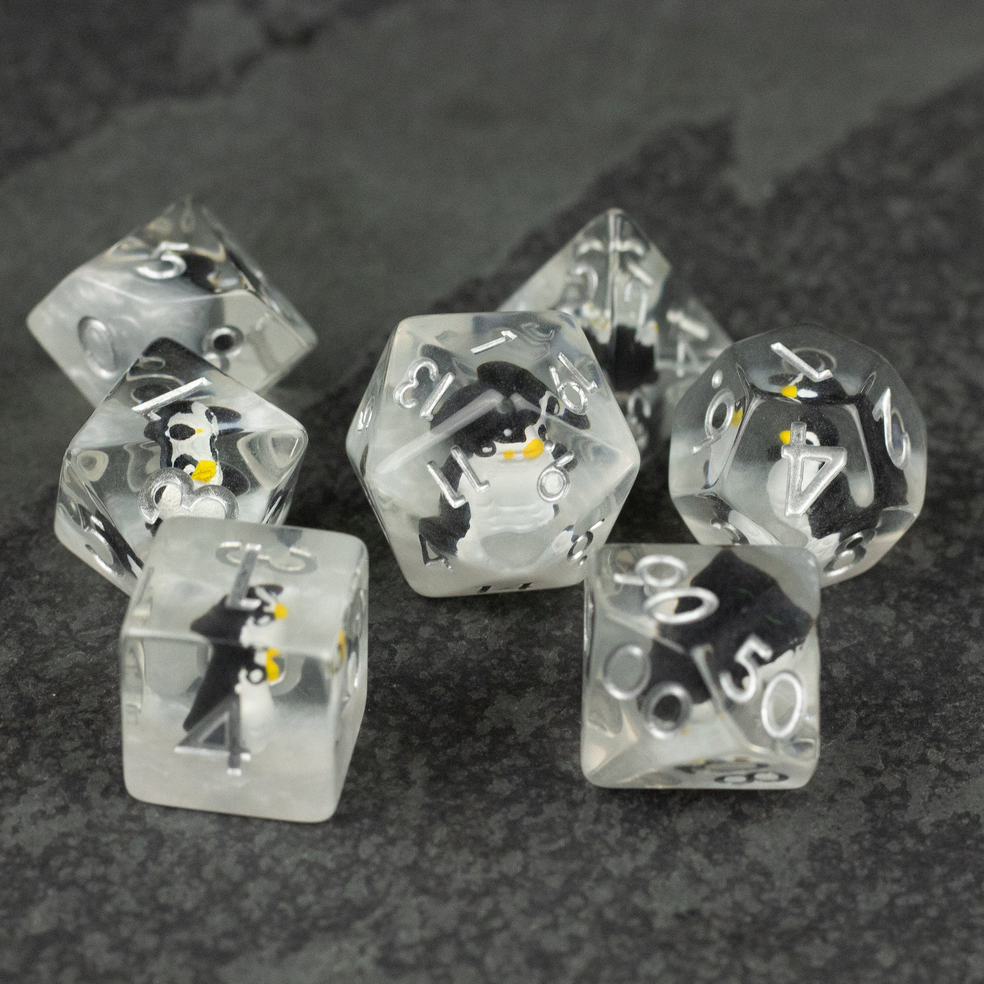 Penguin Dice Set - Set of seven transparent polyhedral dice with embedded small penguin figures, white numbering.