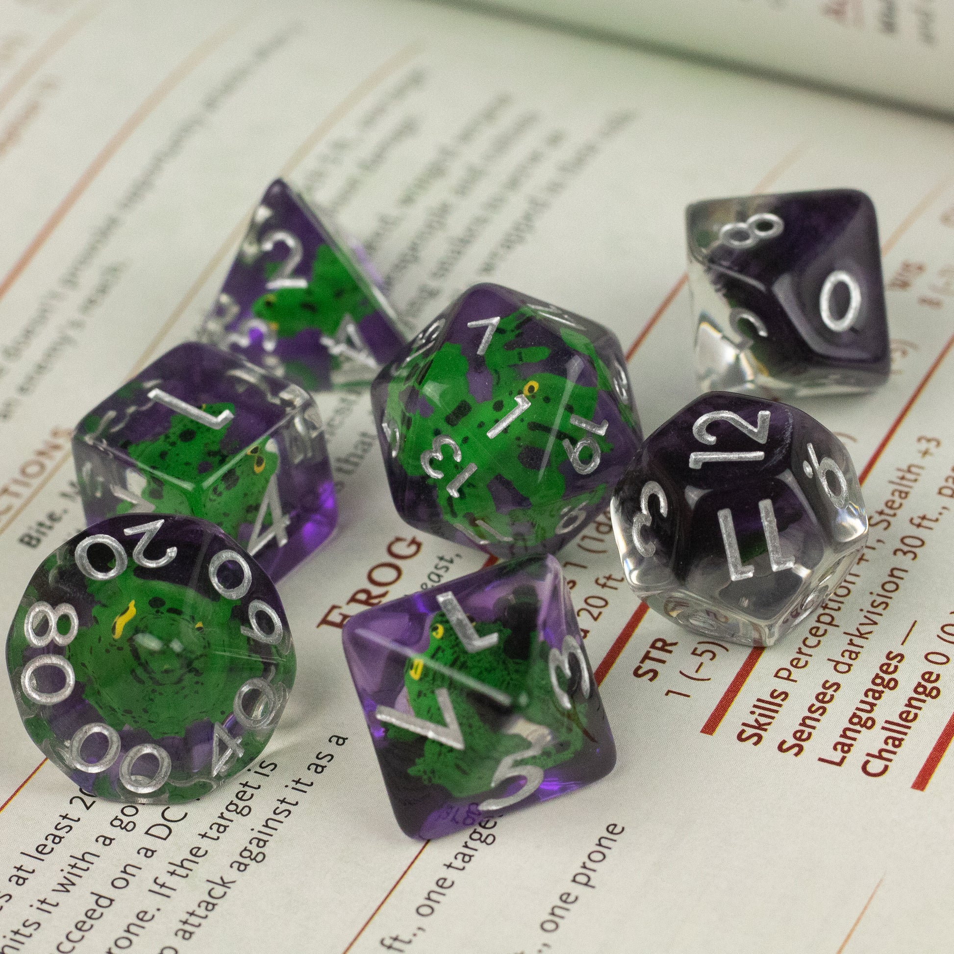 Green Frog Dice Set - Set of seven translucent dice in green and purple with white numbers, including D20, D12, D10, D8, D6, and D4 shapes.