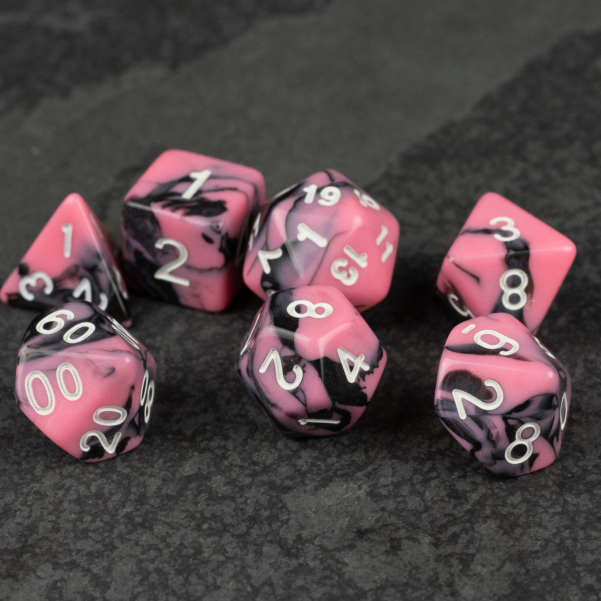 Black & Pink Marbled Dice Set - Set of seven black and pink marbled acrylic dice with white numbering on a dark textured surface.